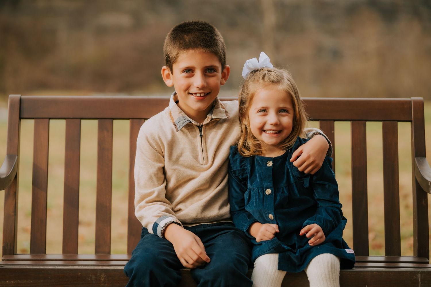 Children sitting together on wooden bench in casual autumn outfits.