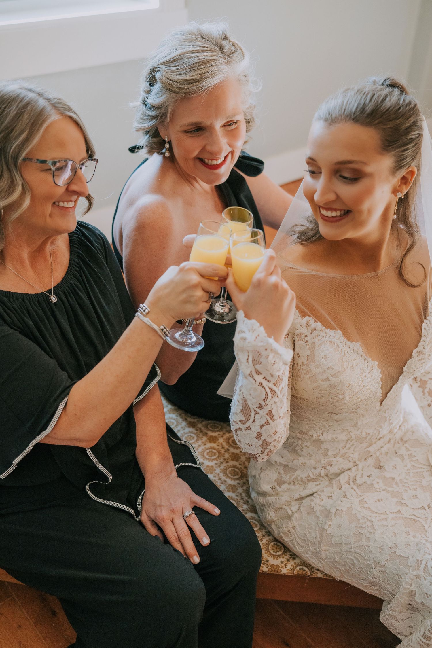 A bride in a lace dress shares joyful moments with loved ones while getting ready for the wedding ceremony.