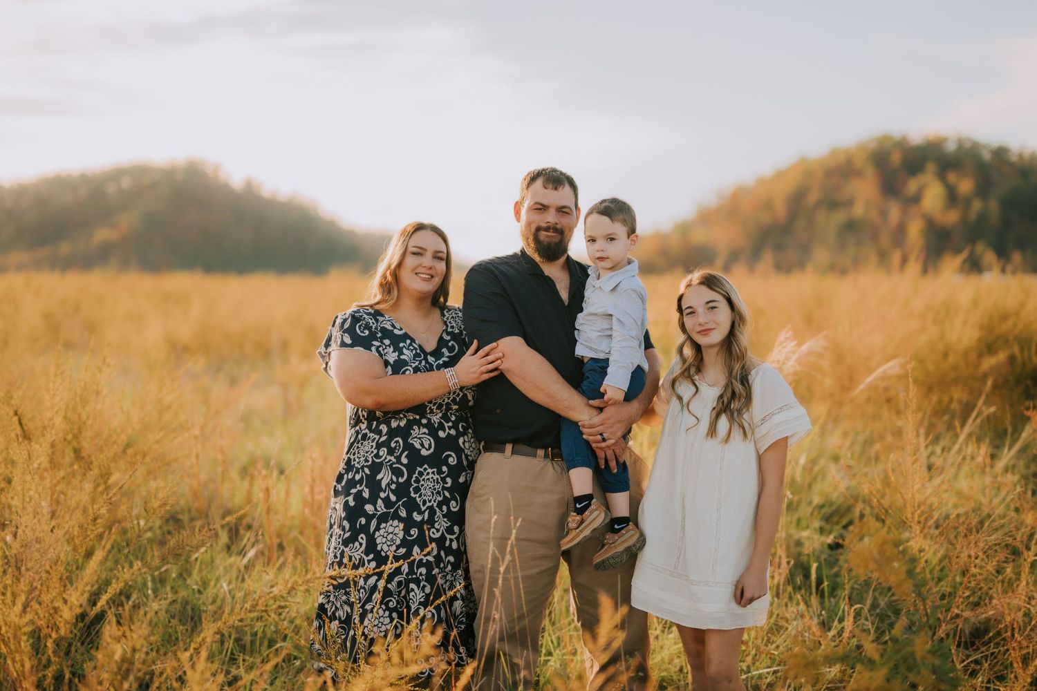 Family walking together in a golden field during sunset with mountains in the background.
