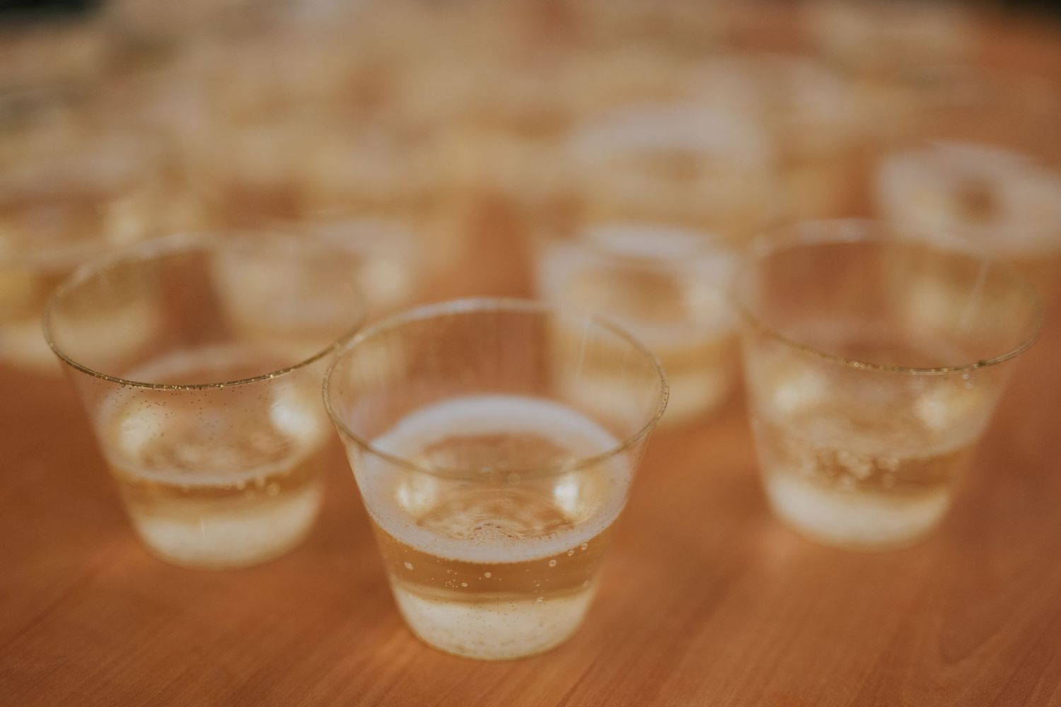Several shot glasses containing layered creamy beige cocktails sit on a wooden surface with soft focus lighting.