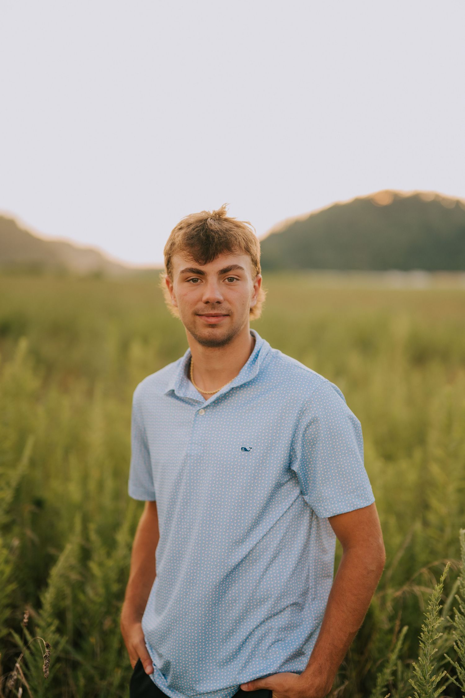 A casual portrait in a light blue polo shirt set against a golden sunset in tall grass.