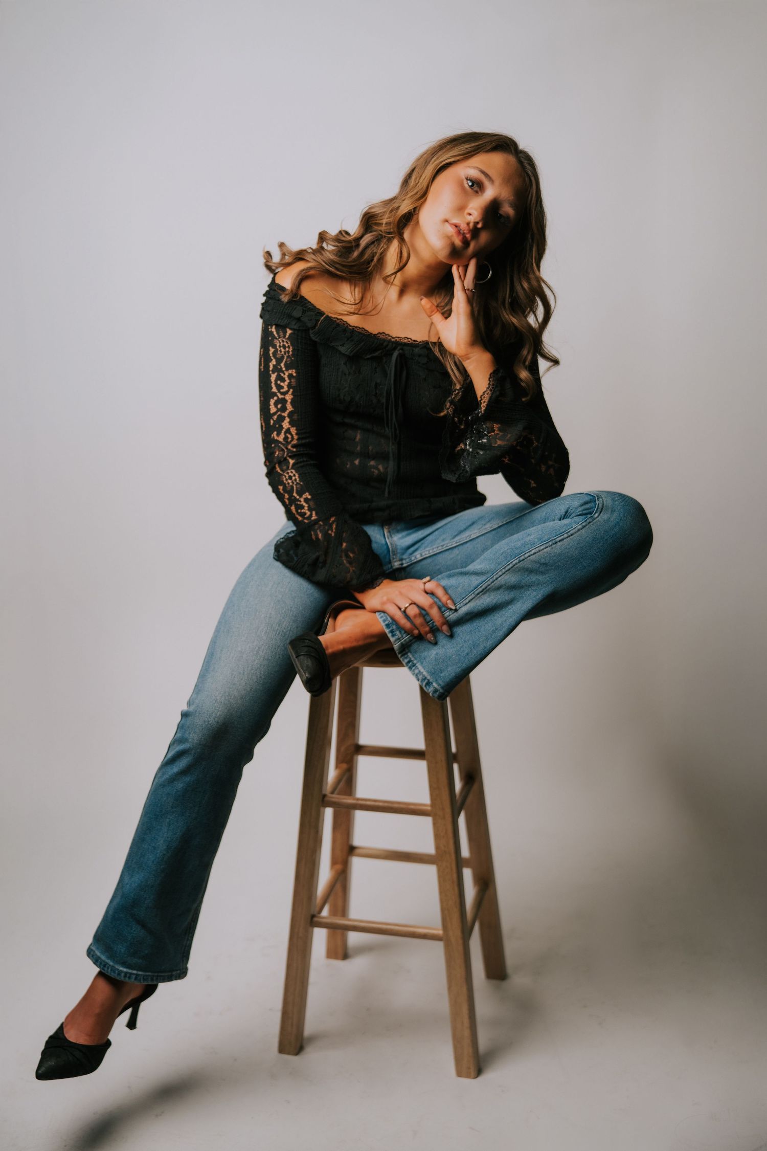 Casual fashion poses on wooden stool wearing cropped black top and blue jeans.