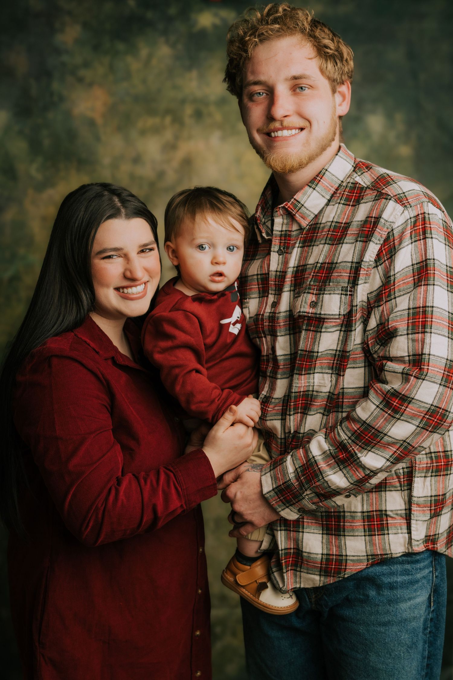 Family portrait with plaid and burgundy outfits against dark backdrop.