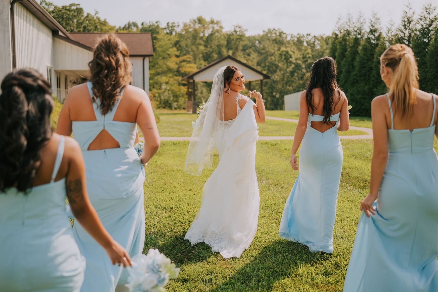 Bridesmaids in matching blue dresses stand with the bride outdoors on a sunny day.