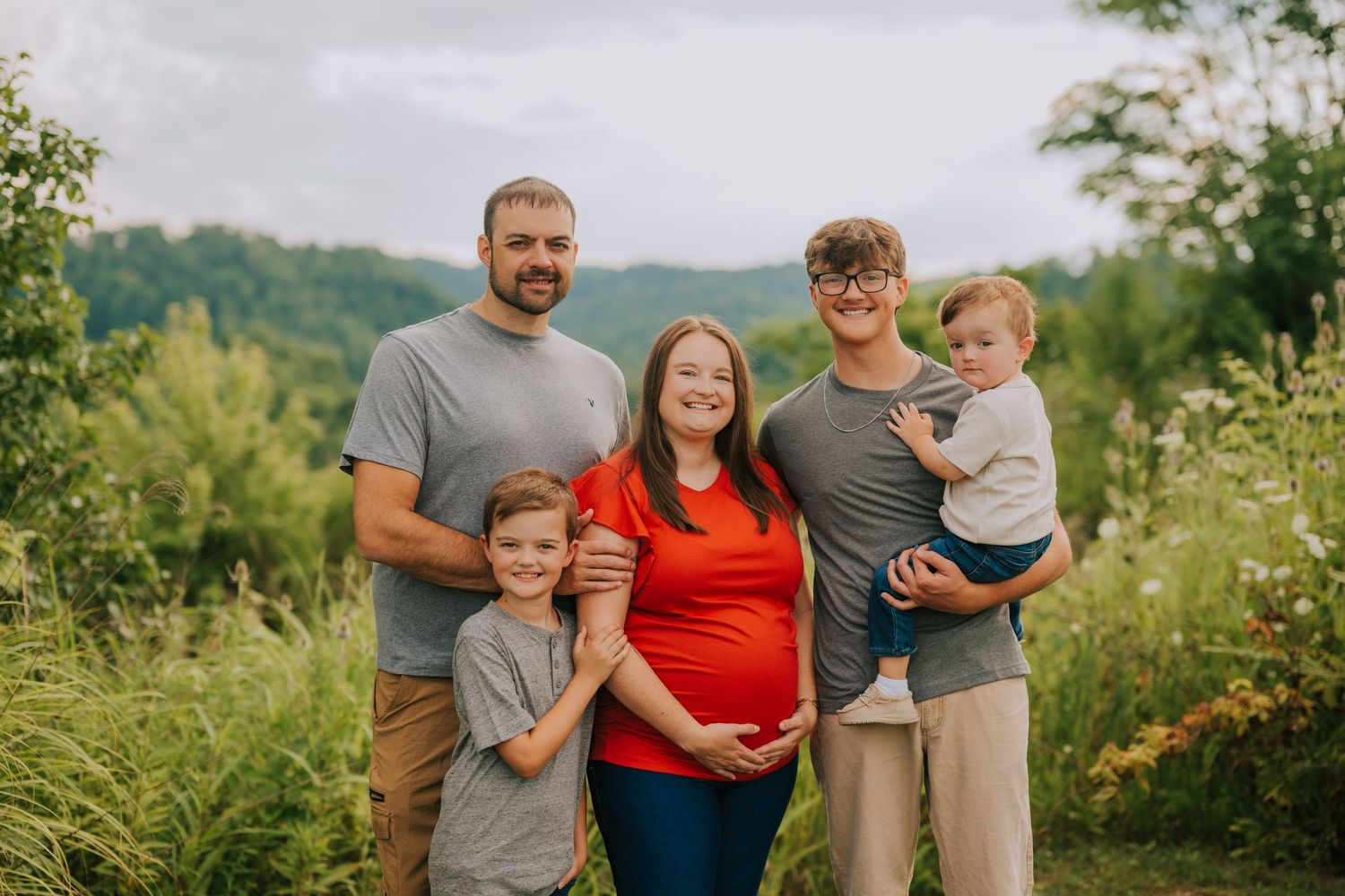 Family group photo session in lush green summer landscape.