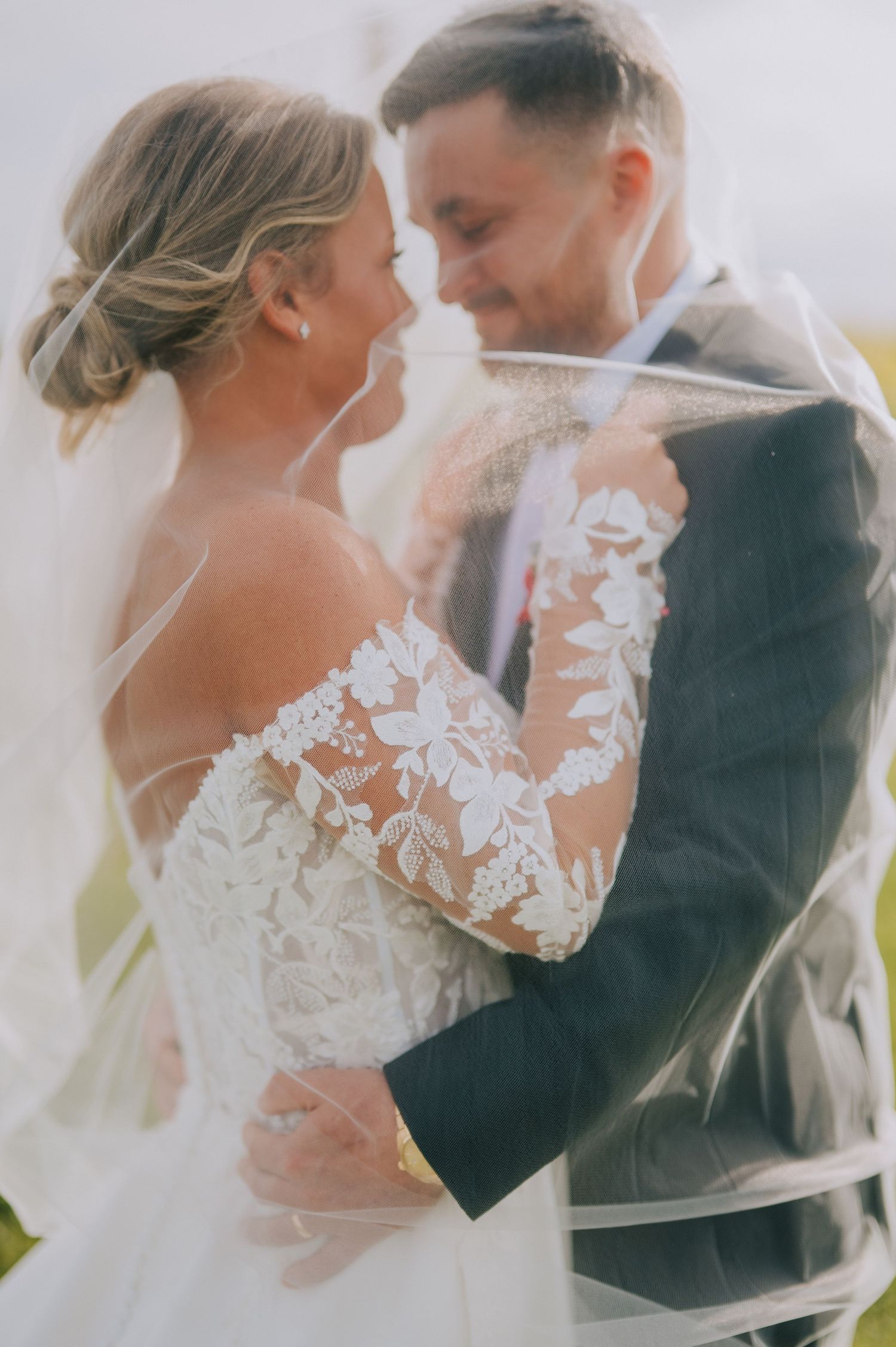 Romantic moment between newlyweds captured through flowing veil in soft light.