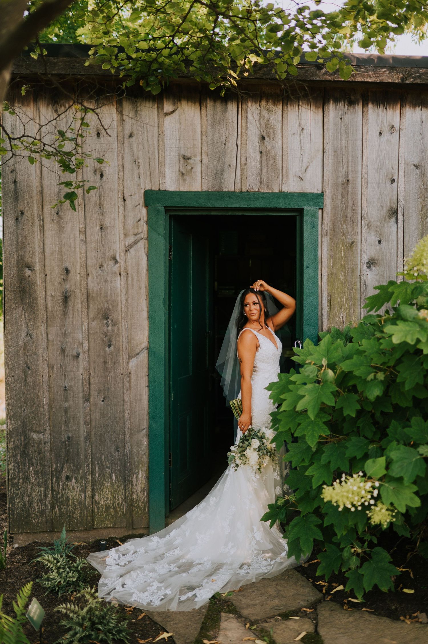 White wedding dress with long train framed in rustic wooden doorway with green trim.
