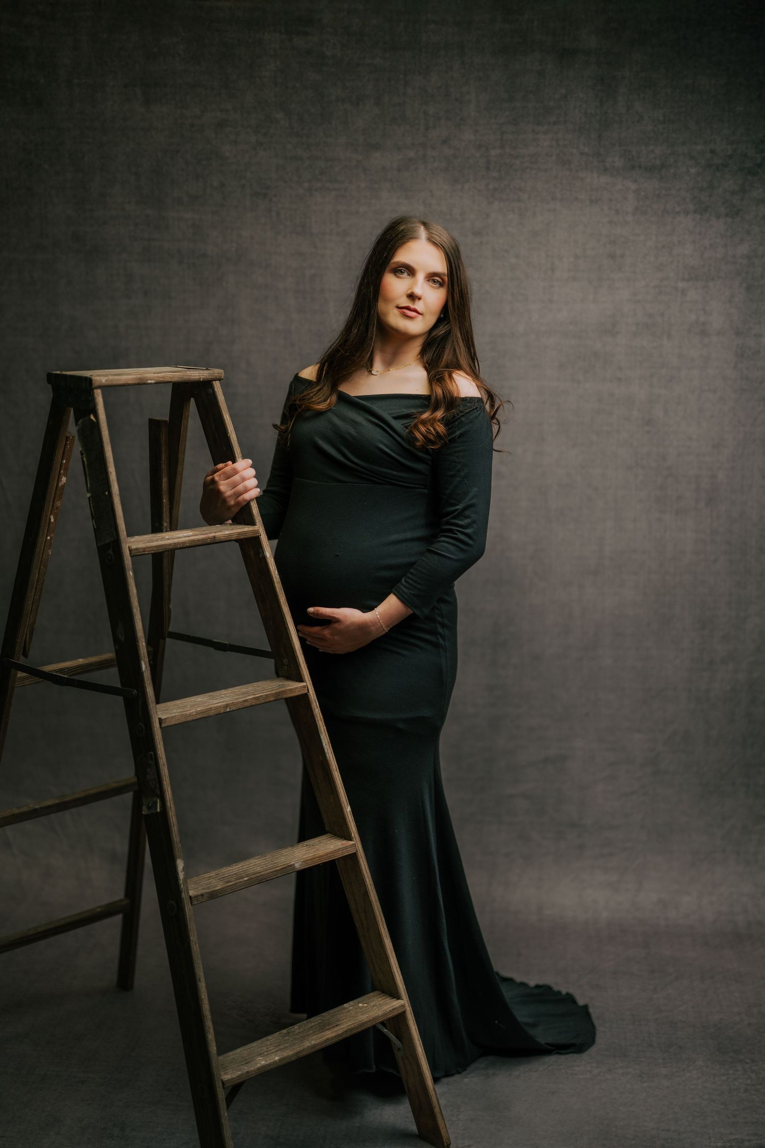 Artistic portrait series featuring a black dress against a dark backdrop with a wooden ladder prop.