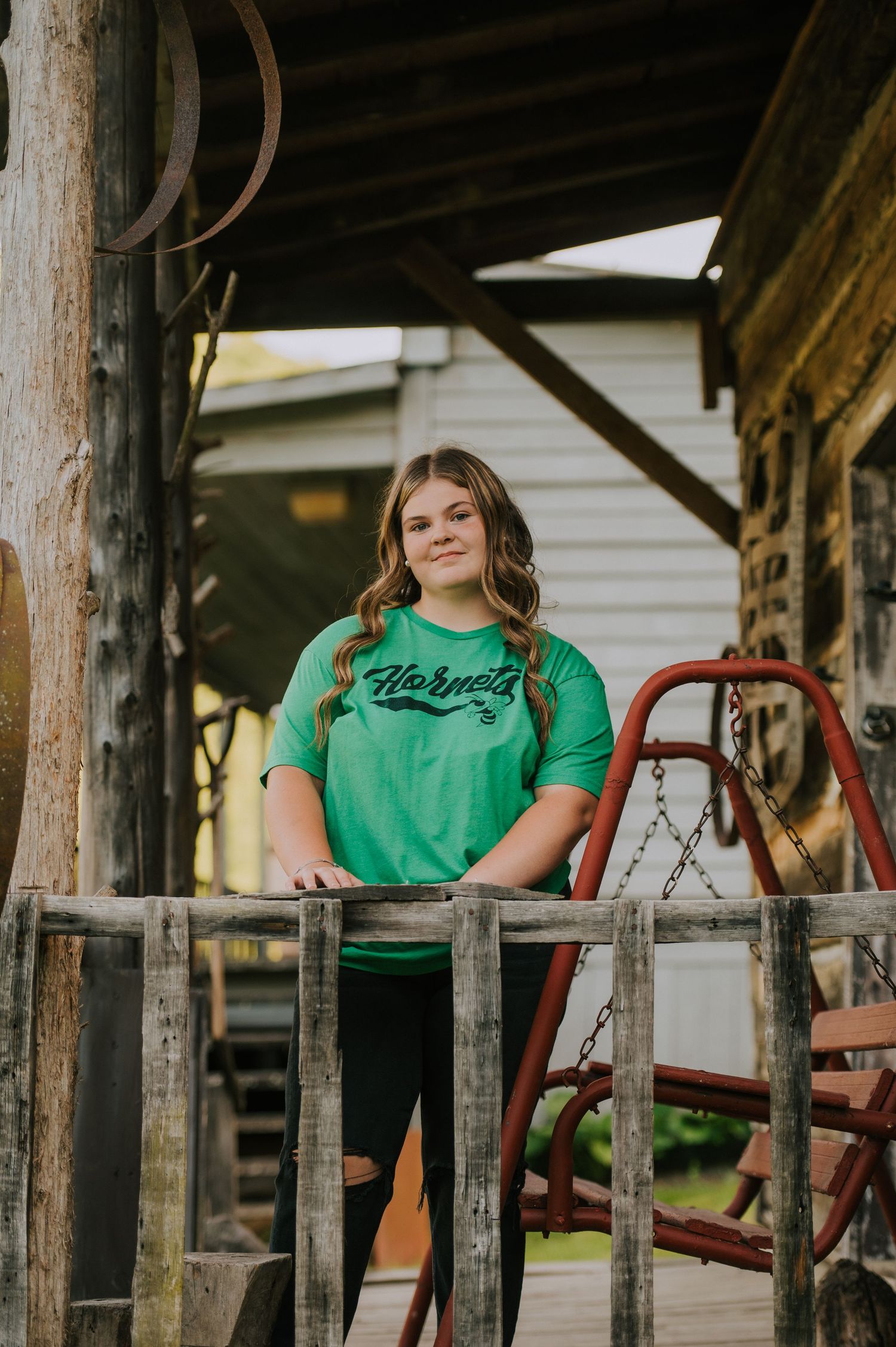 A person in green sits on wooden swings at a rustic covered porch.