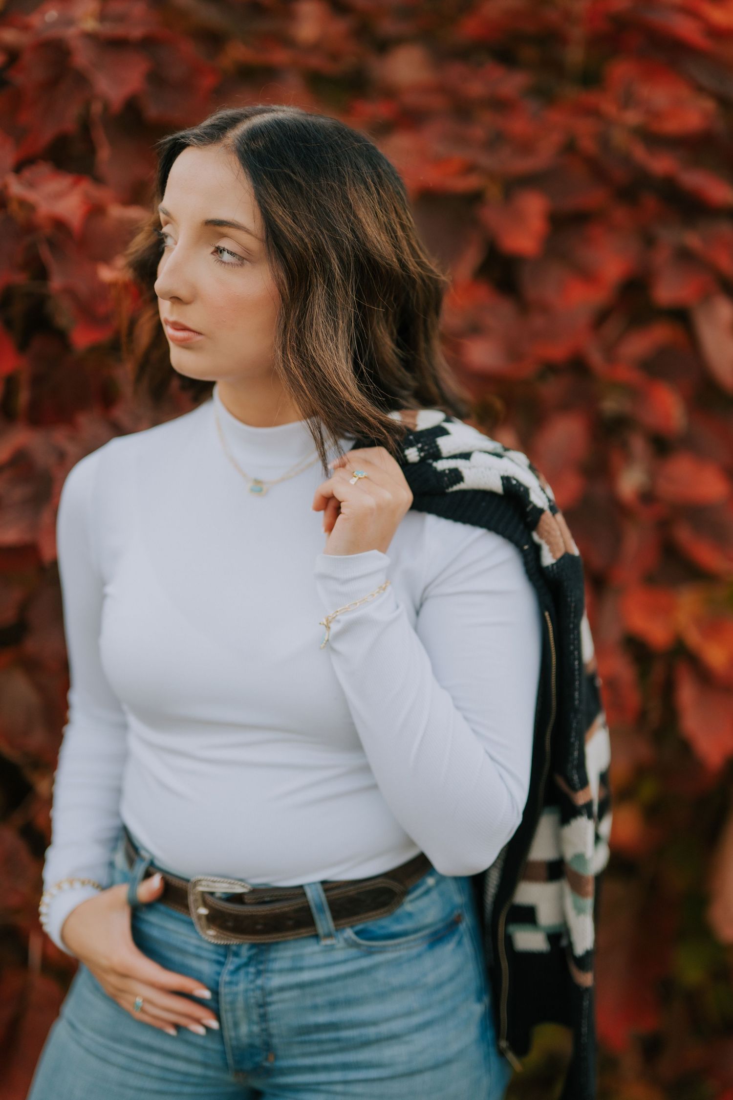 Fashion portrait against red autumn foliage featuring white sweater and denim outfit.