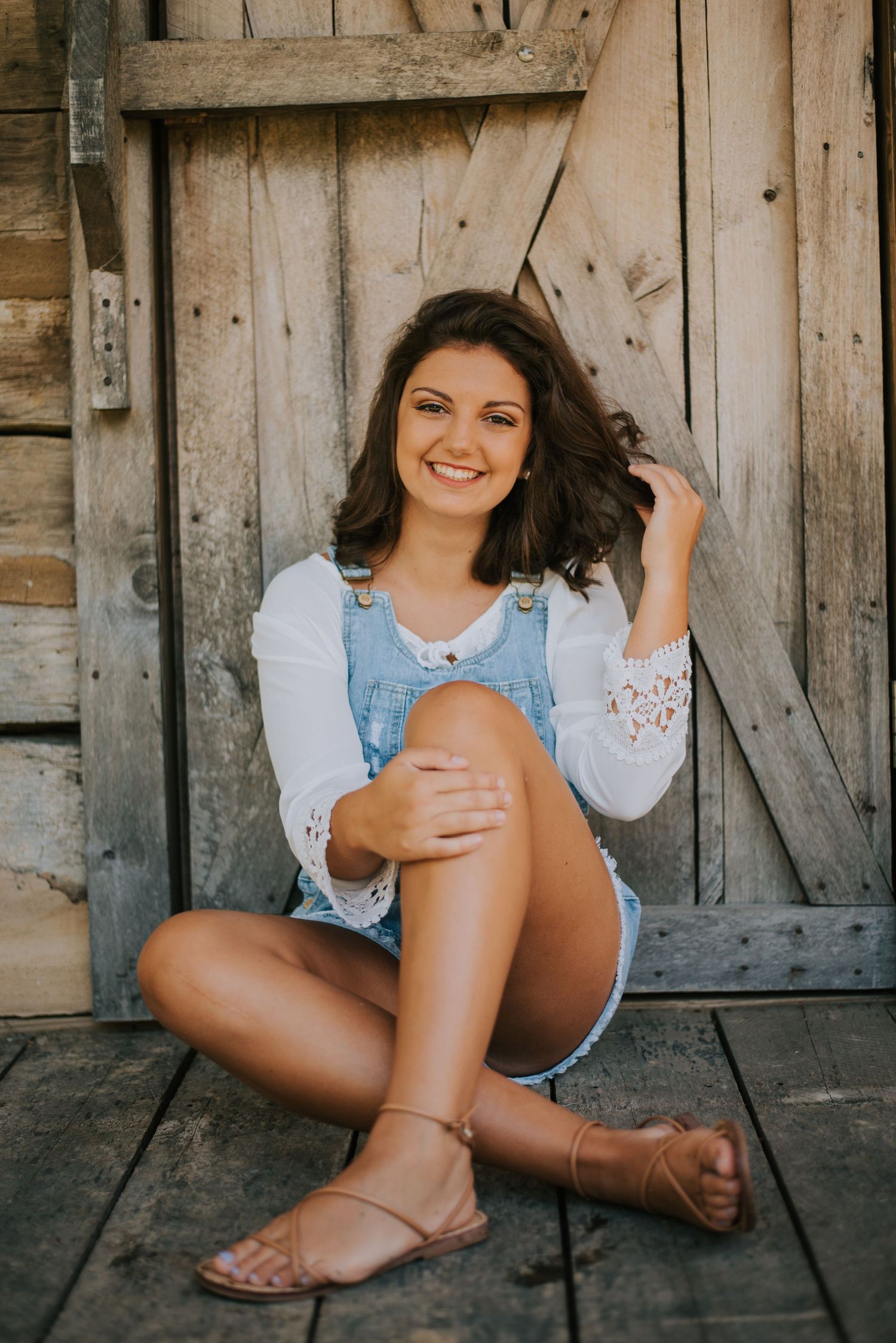 A rustic wooden barn wall serves as a backdrop for a casual summer photoshoot.
