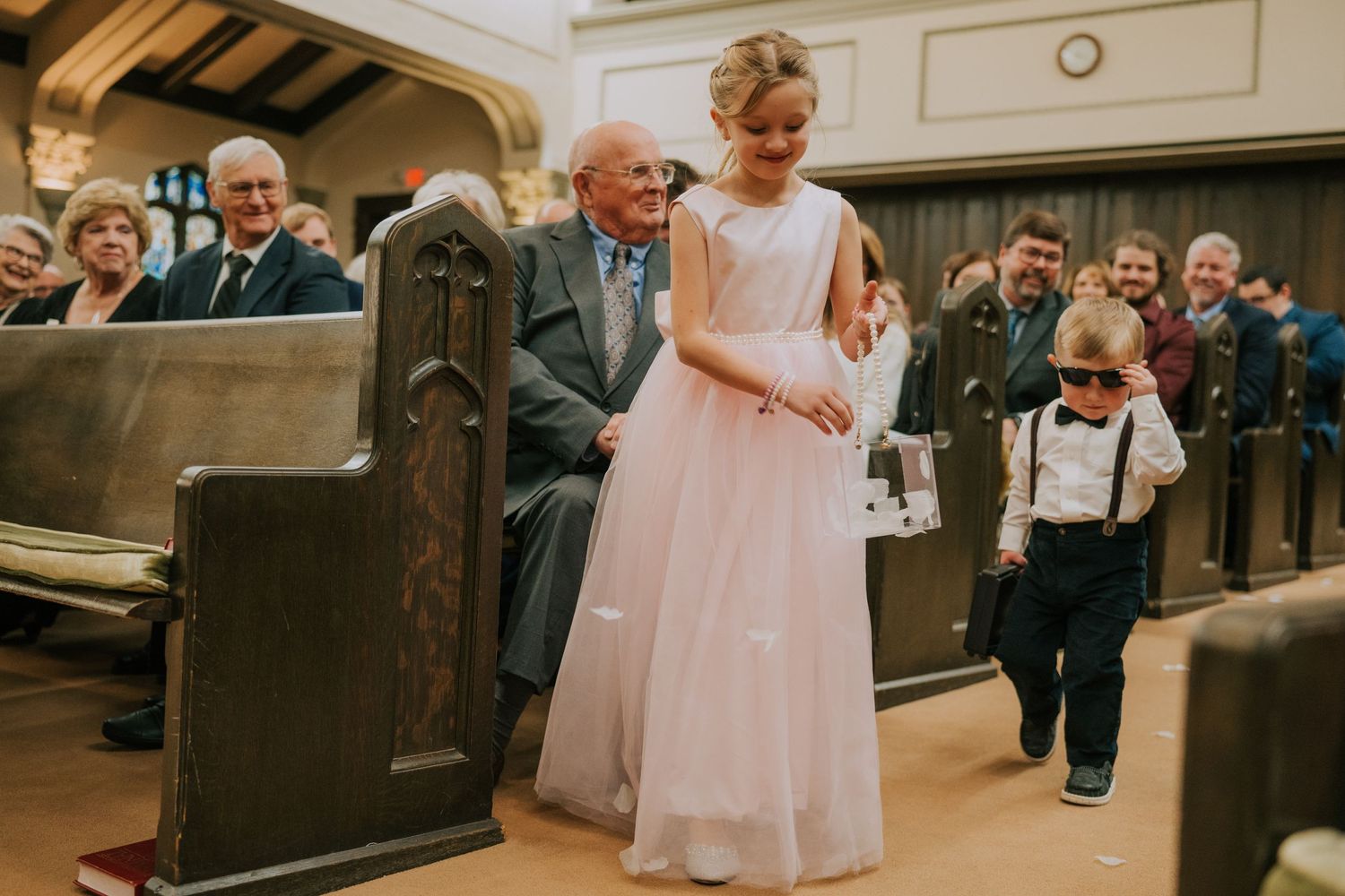 Young attendants walk down the aisle of a traditional church during a wedding ceremony.