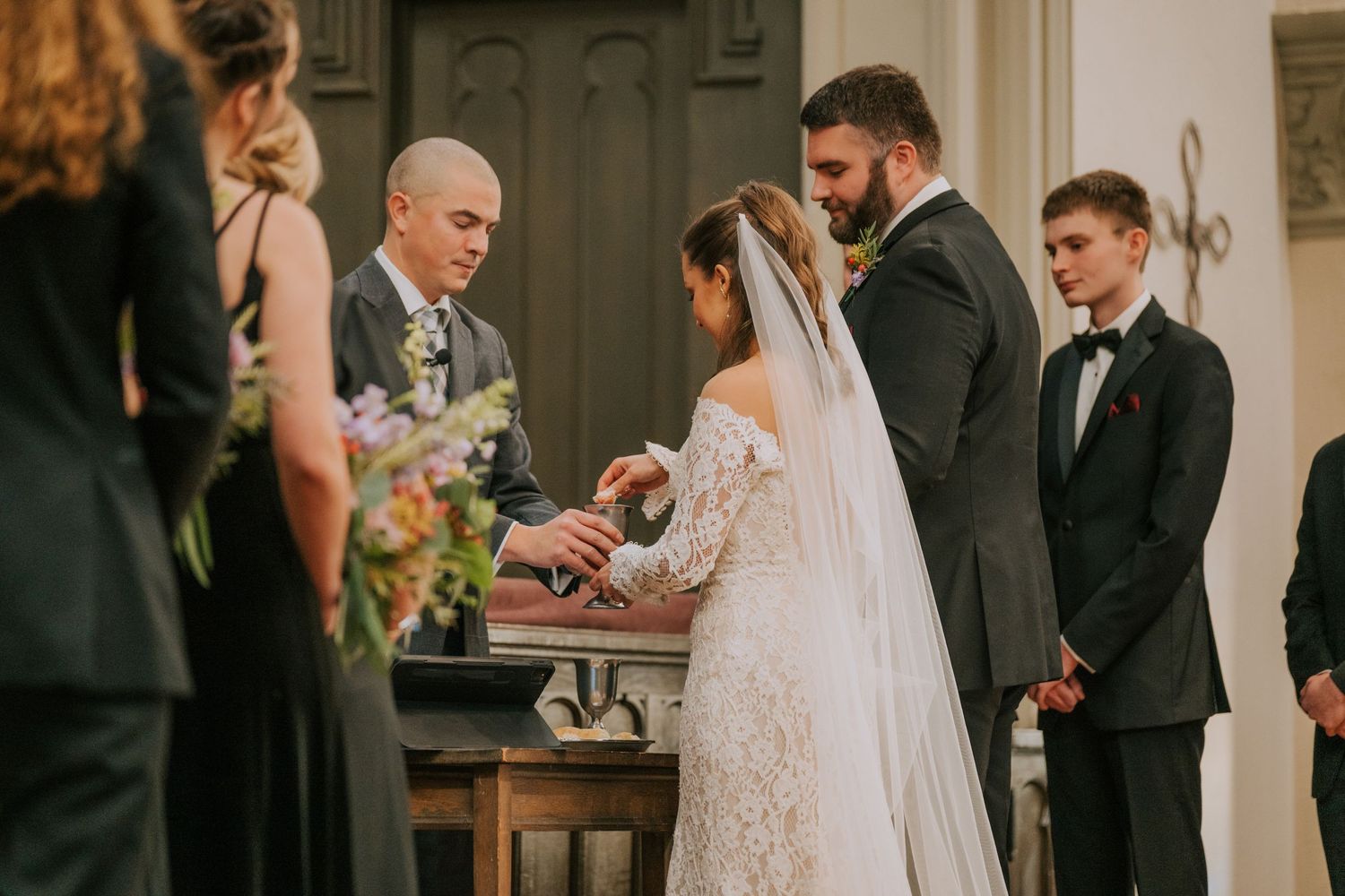 Wedding ceremony being conducted at an altar with lace-gowned bride in traditional white veil and elegant church interior.