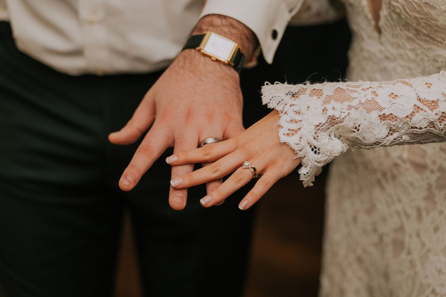 Close-up of newlyweds' hands showing off their wedding rings with lace sleeve detail.