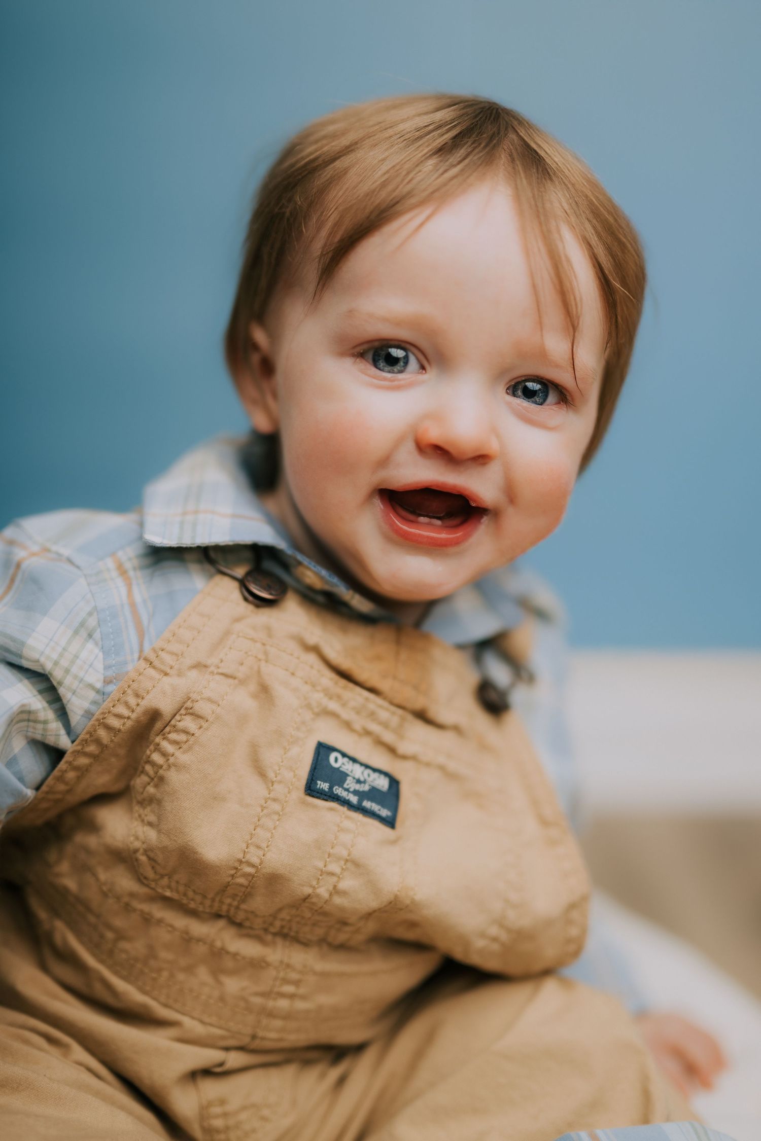 Baby wearing tan overalls against light blue background.