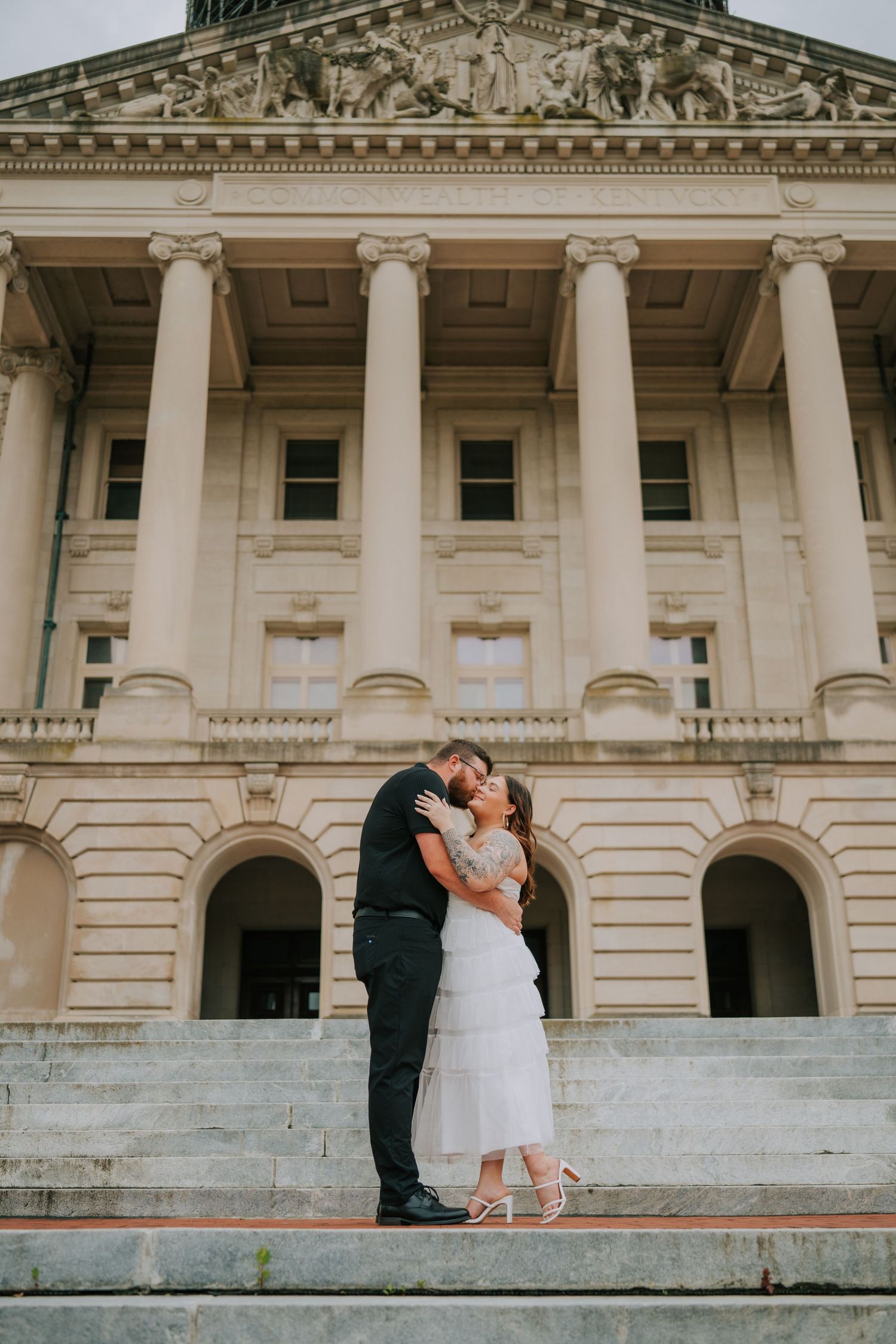 A couple shares a romantic moment in front of a grand neoclassical building with white columns.