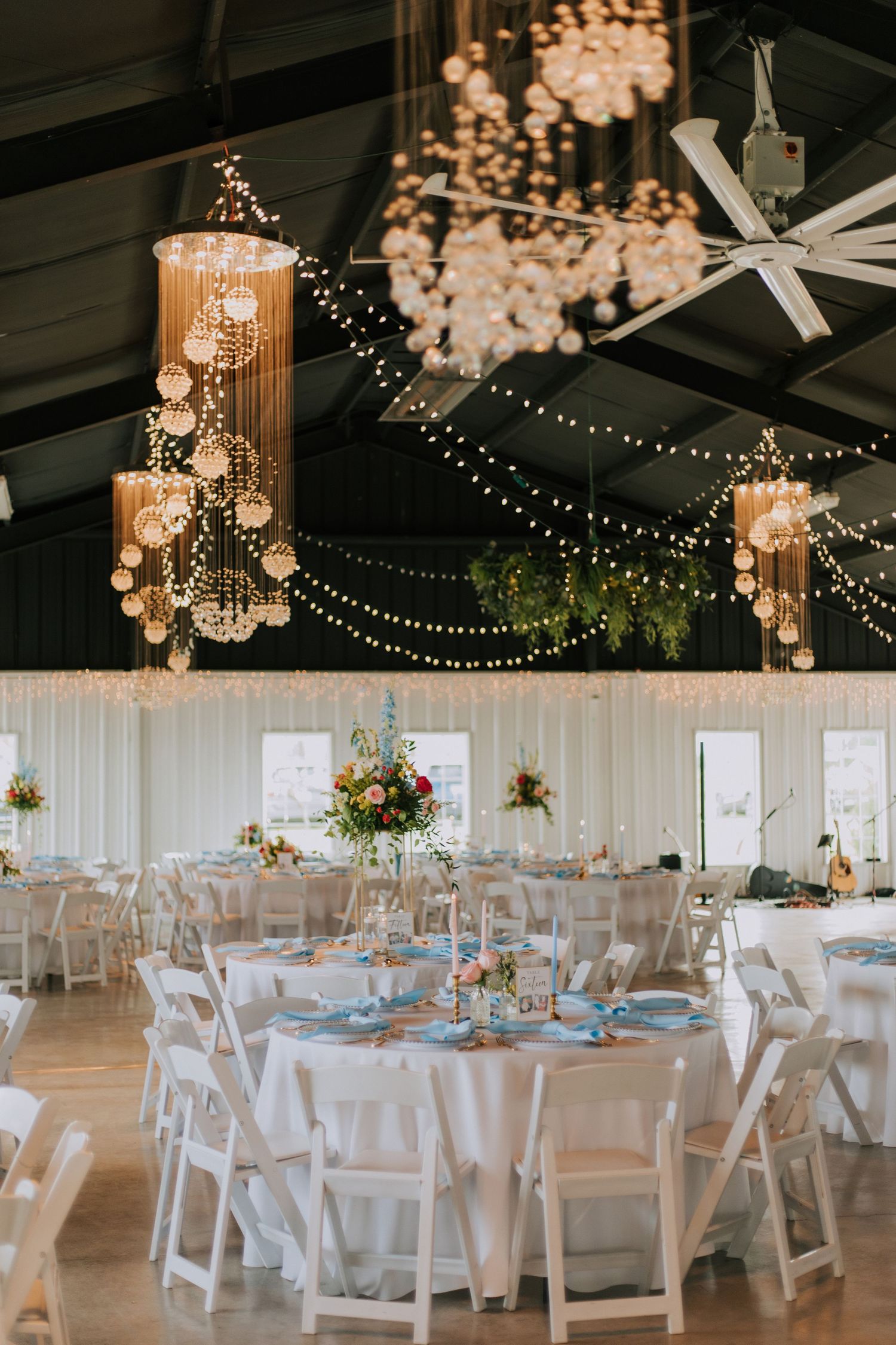 Elegant reception hall decorated with crystal chandeliers and string lights over white round tables.