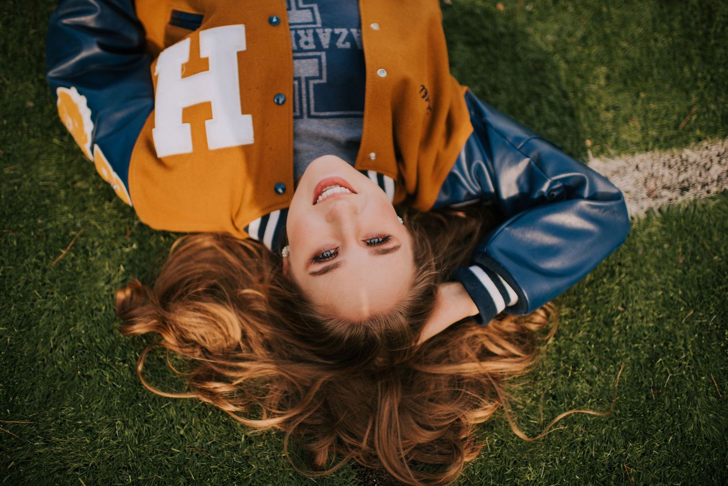 Person in sports jersey lying on grass field during golden hour photography session.