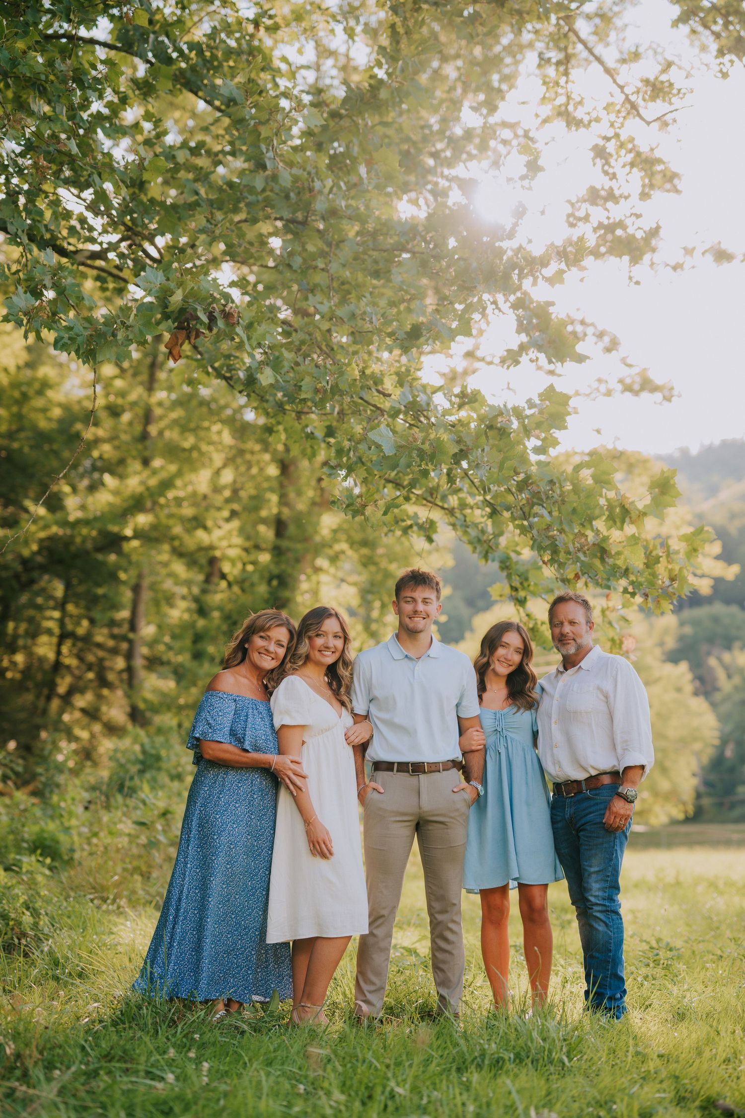 Family gathering posed together in a sun-dappled meadow on a summer afternoon.