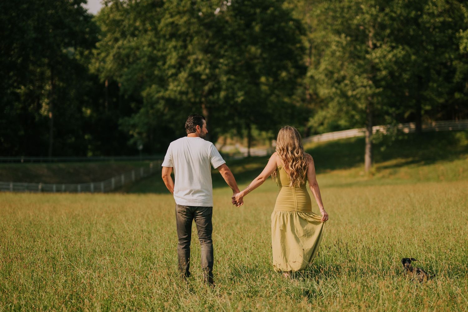 Couple walking hand in hand through a sunlit grassy field at golden hour.