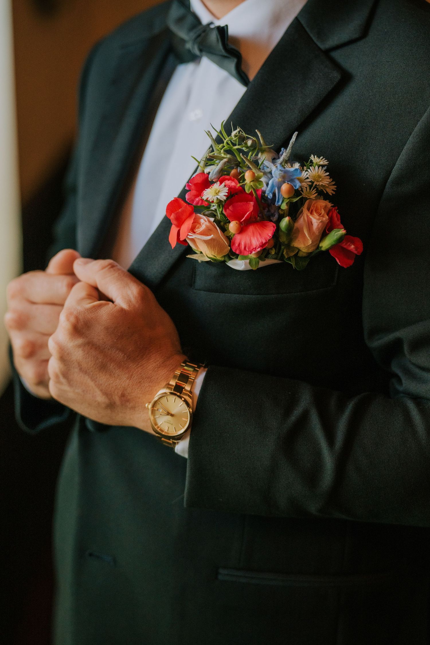 Close-up of boutonniere and suit details with colorful flowers and gold watch.