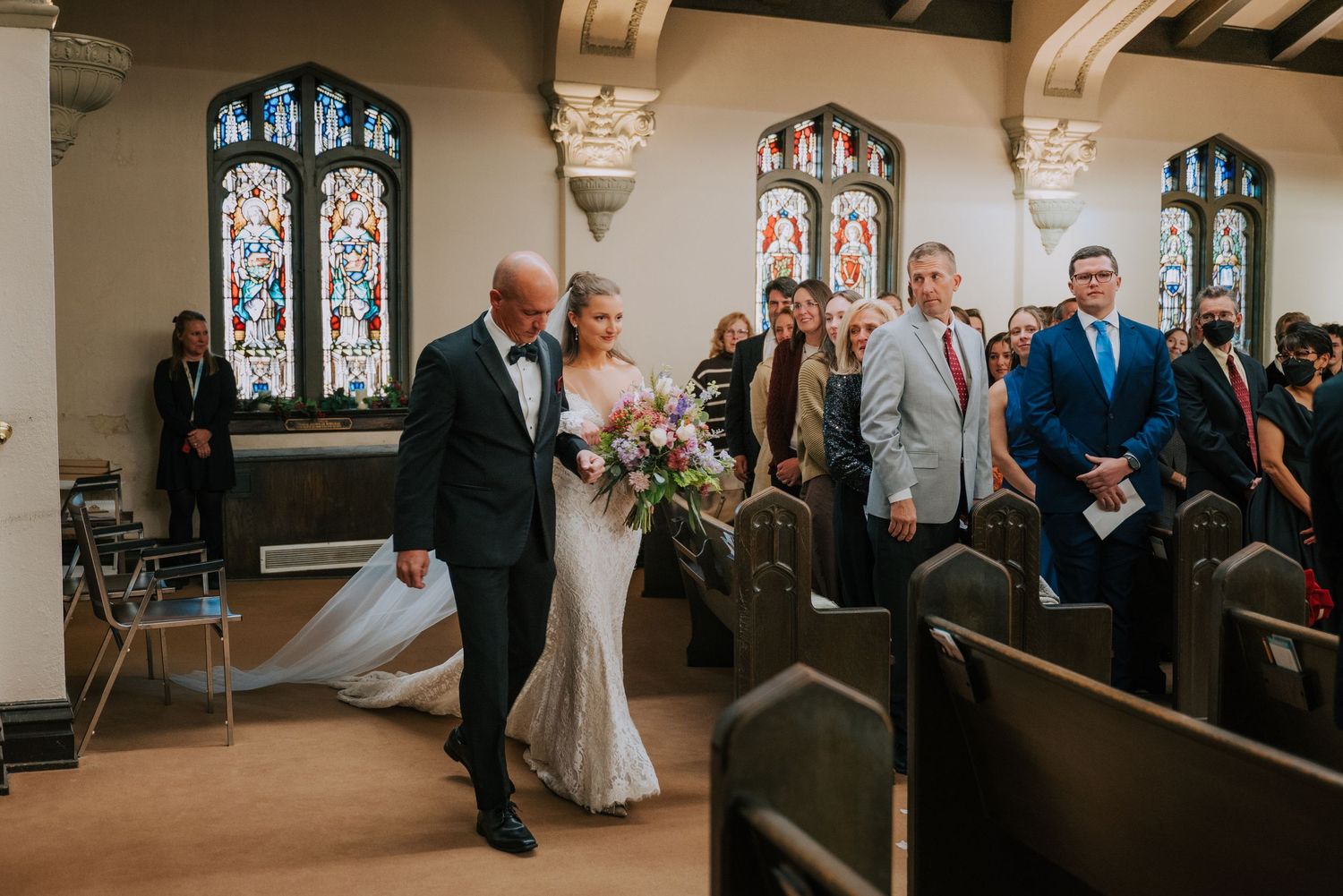 Wedding ceremony taking place in a historic church chapel with stained glass windows and wooden pews.