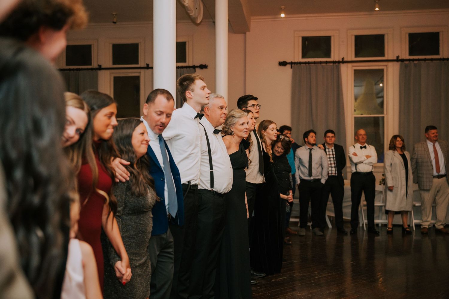 Wedding guests lined up in formal attire participating in group dance at reception.