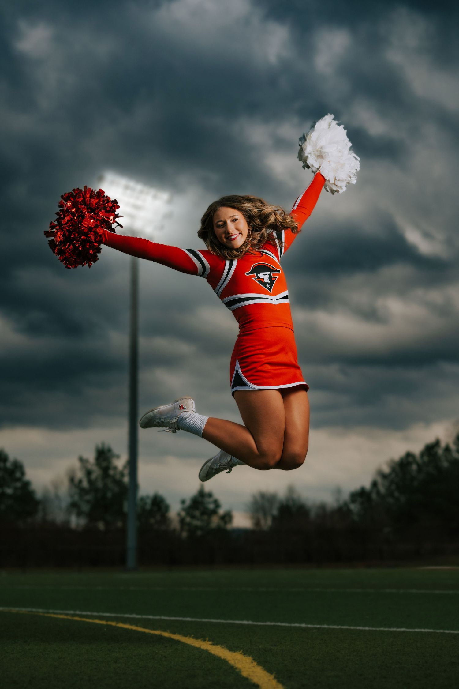 A cheerleader performs a dynamic jump sequence against a dramatic stormy sky background with red and white uniform.