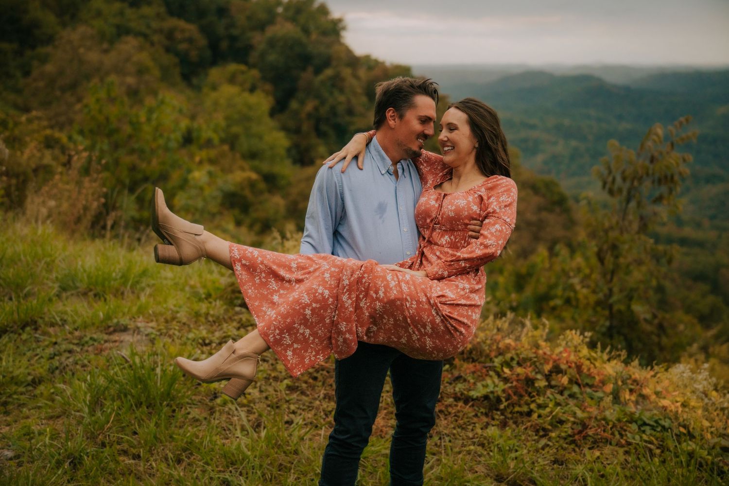 A couple embraces on a hilltop overlooking mountain vistas during golden hour.