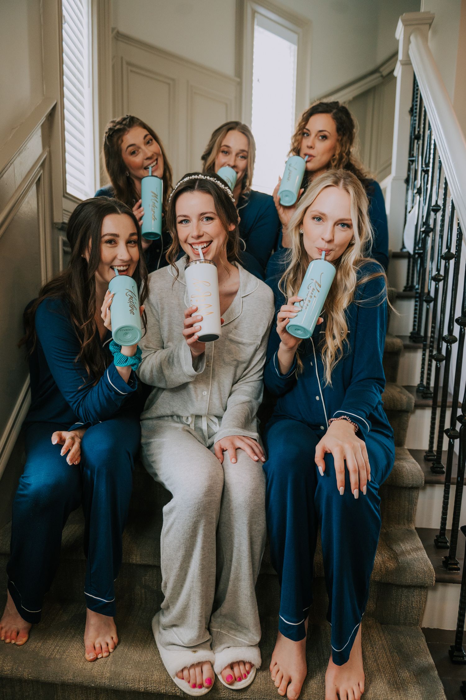 Group wearing navy and gray loungewear sitting on stairs holding blue tumblers.