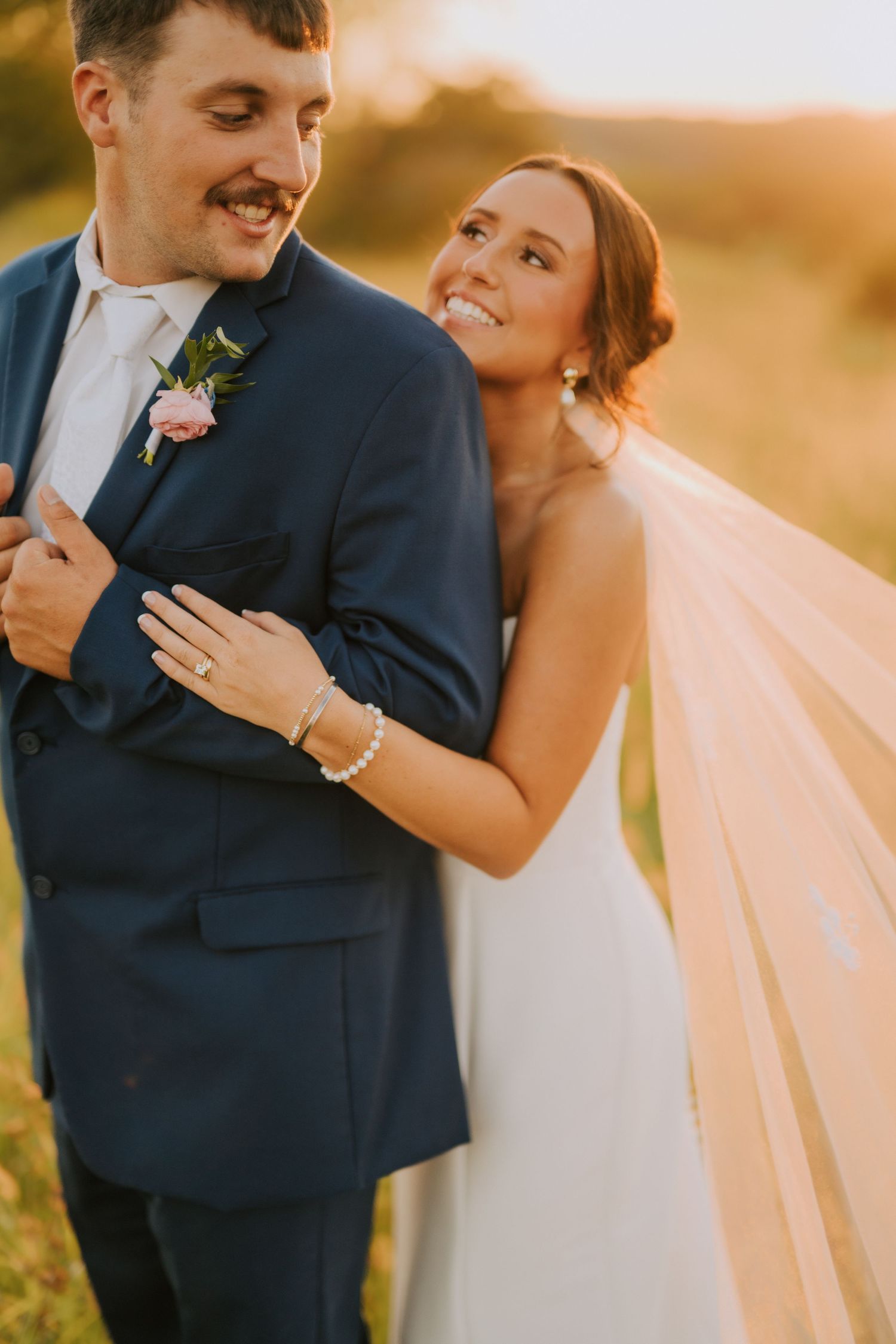 Elegant wedding couple embracing in a field during golden hour.