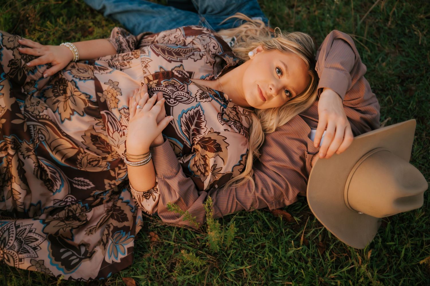 Woman in flowing dress lies gracefully in tall grass during sunset.