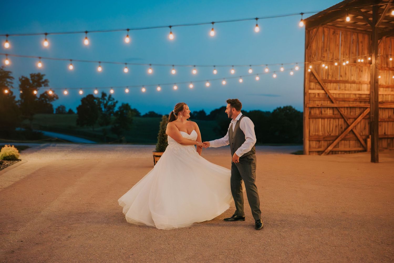 Evening reception scene with string lights glowing against a rustic barn backdrop.