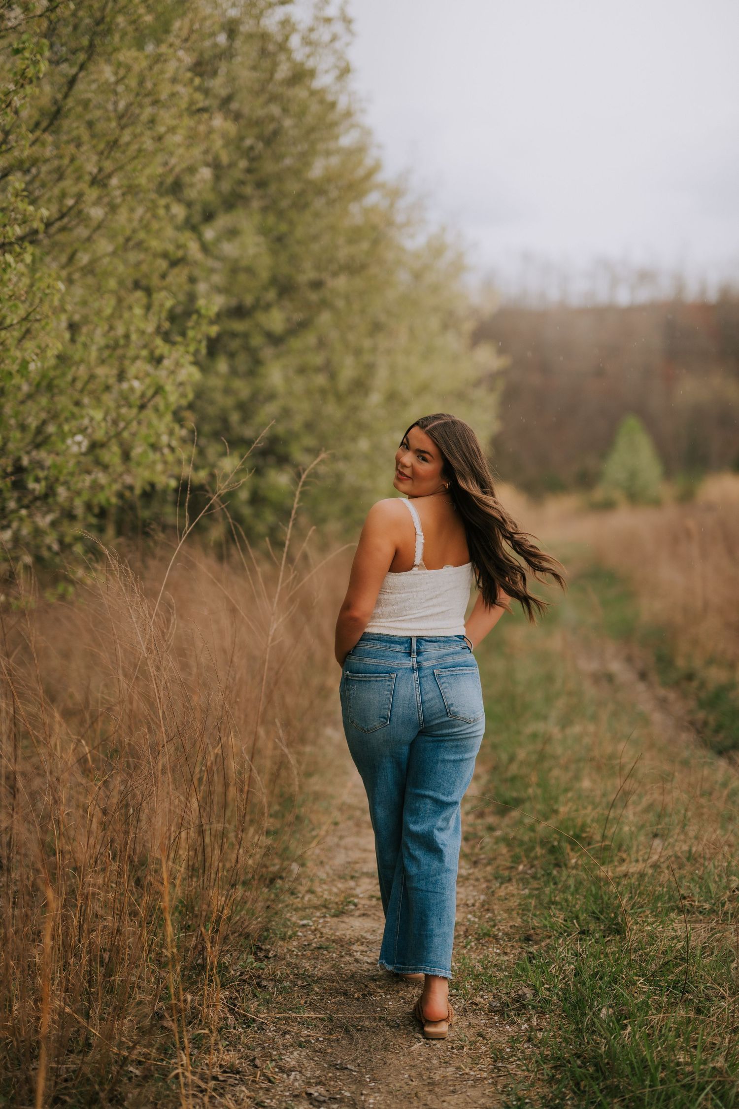 Back view of person in jeans walking through natural pathway with trees.