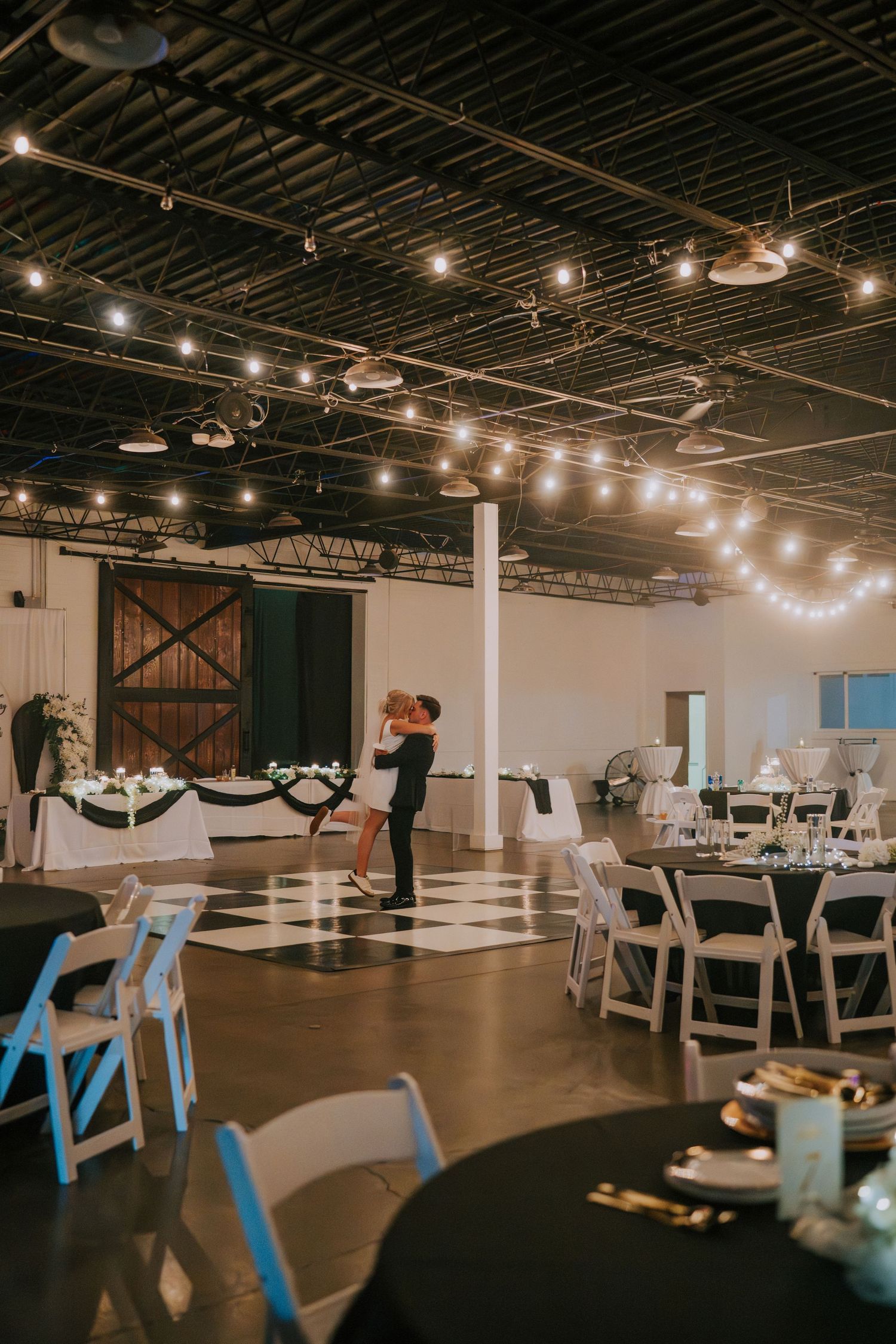 Modern industrial wedding venue with string lights and white table settings.
