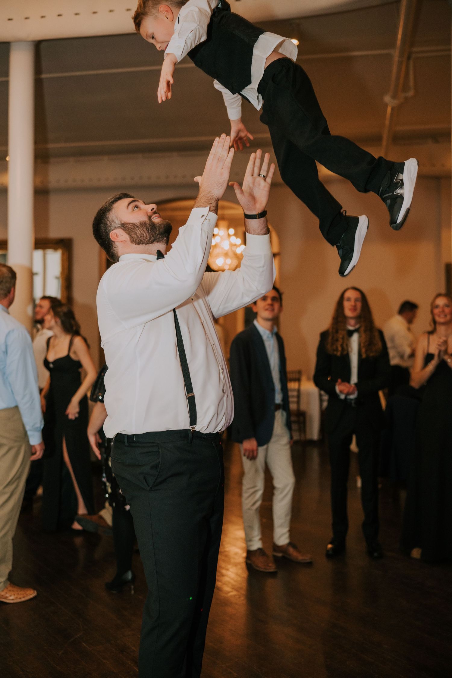 Wedding guests dancing and lifting someone during a lively reception celebration.