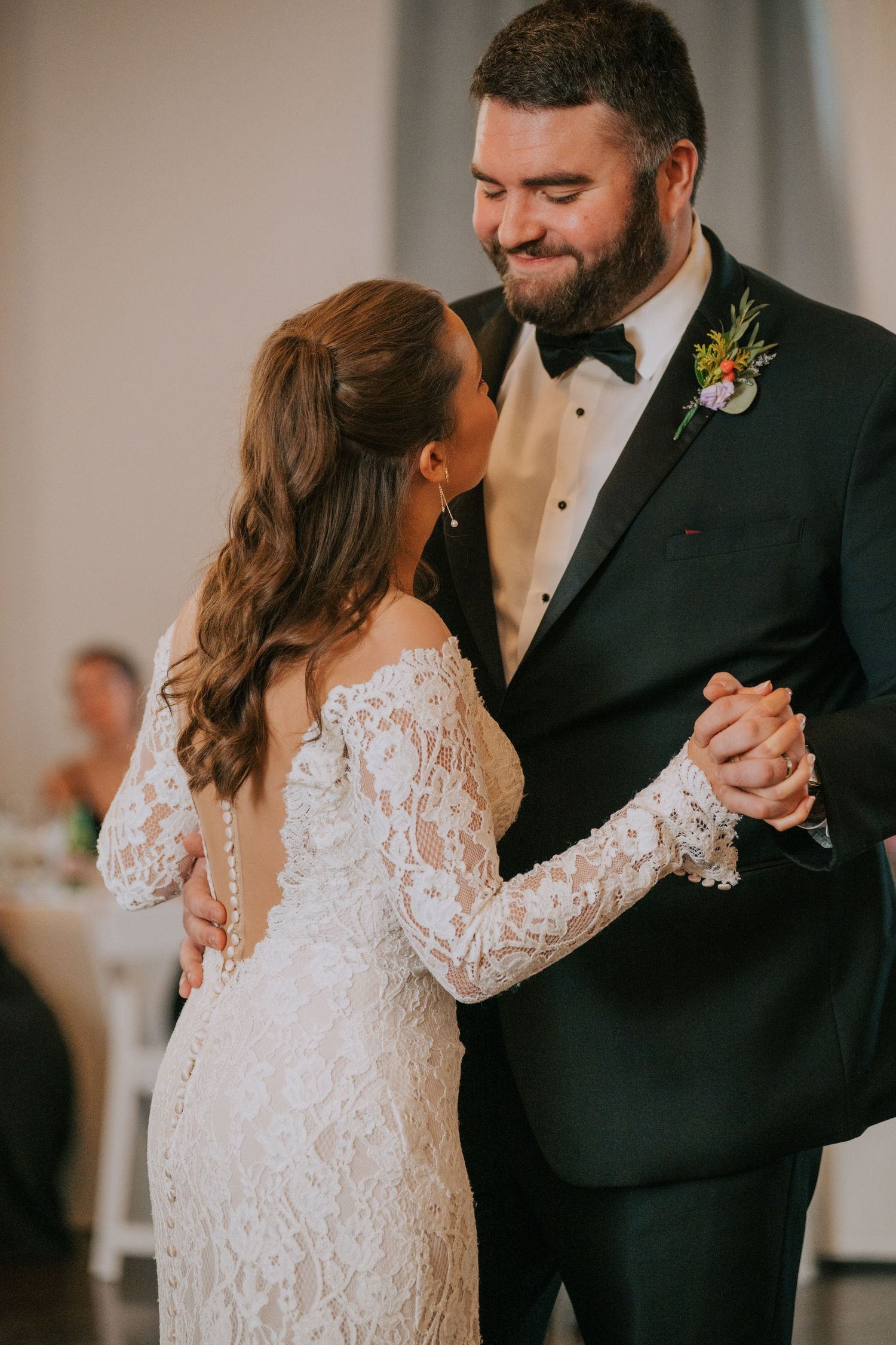 Newlyweds share their first dance at wedding reception, bride wearing lace long sleeve gown and groom in black tuxedo.