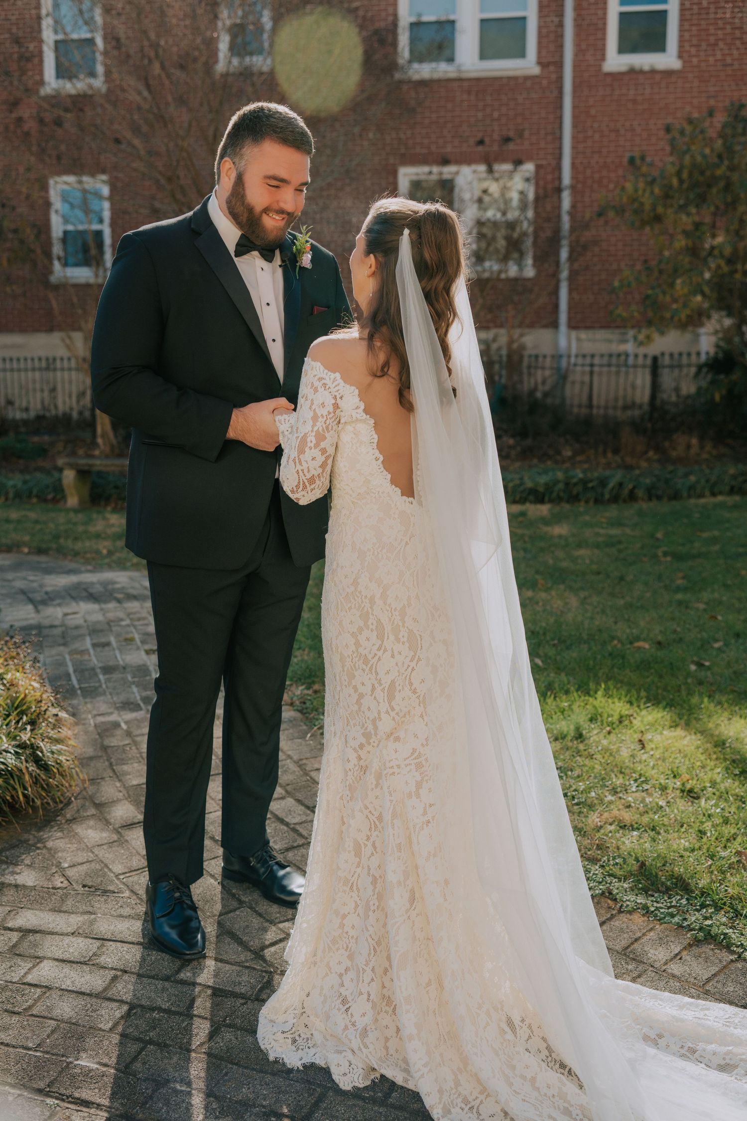 A romantic moment between a couple in wedding attire standing on brick pavers in front of a brick building.