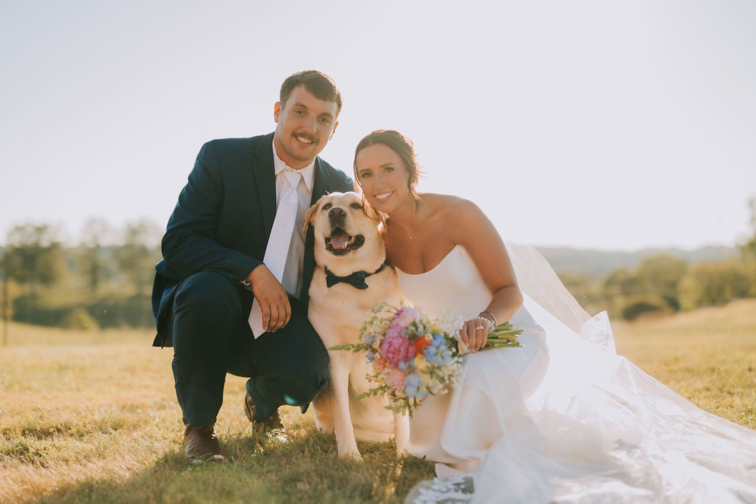 Romantic wedding couple poses in golden field during sunset with colorful bouquet.