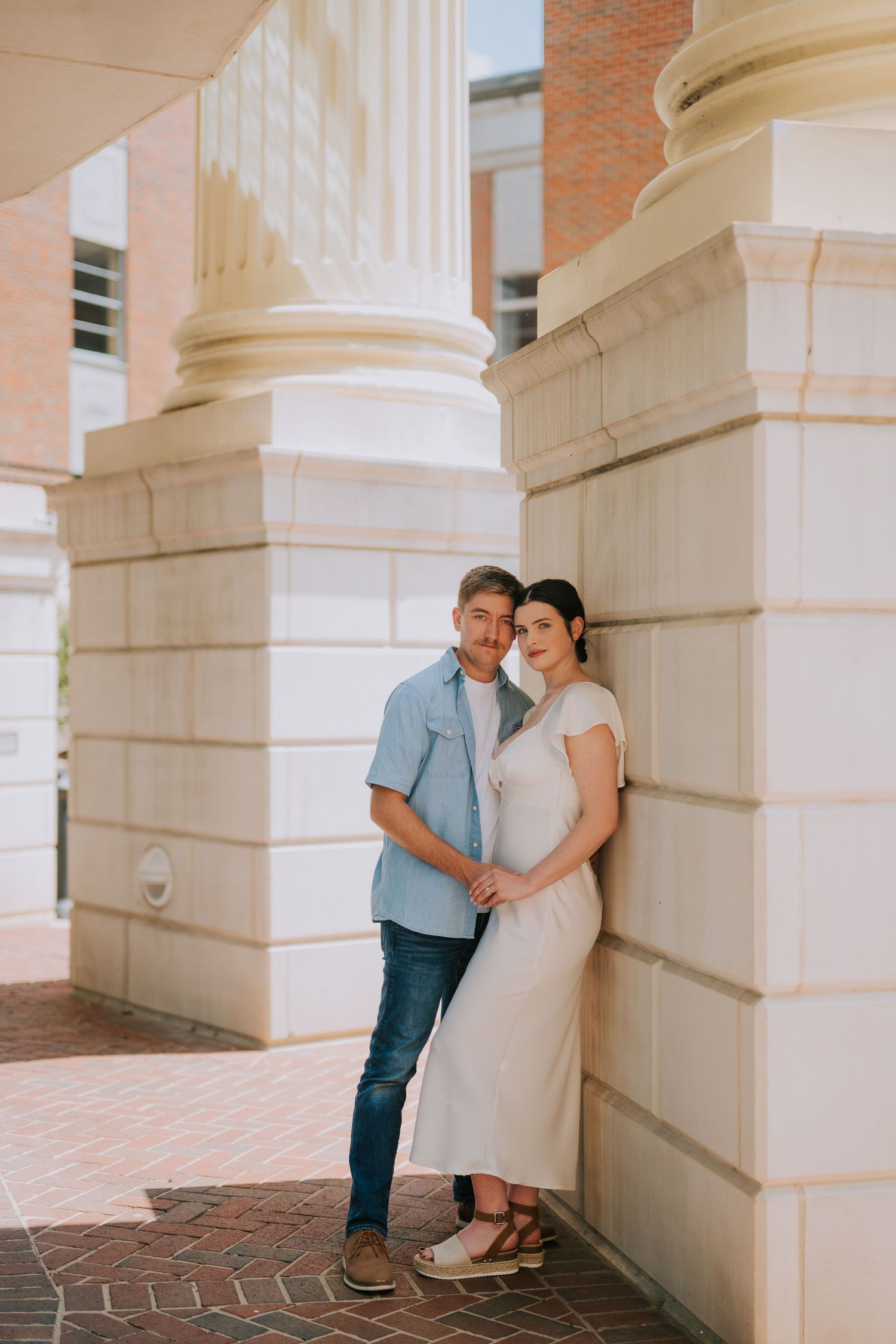 Couple embracing between elegant white stone columns in a romantic architectural setting.