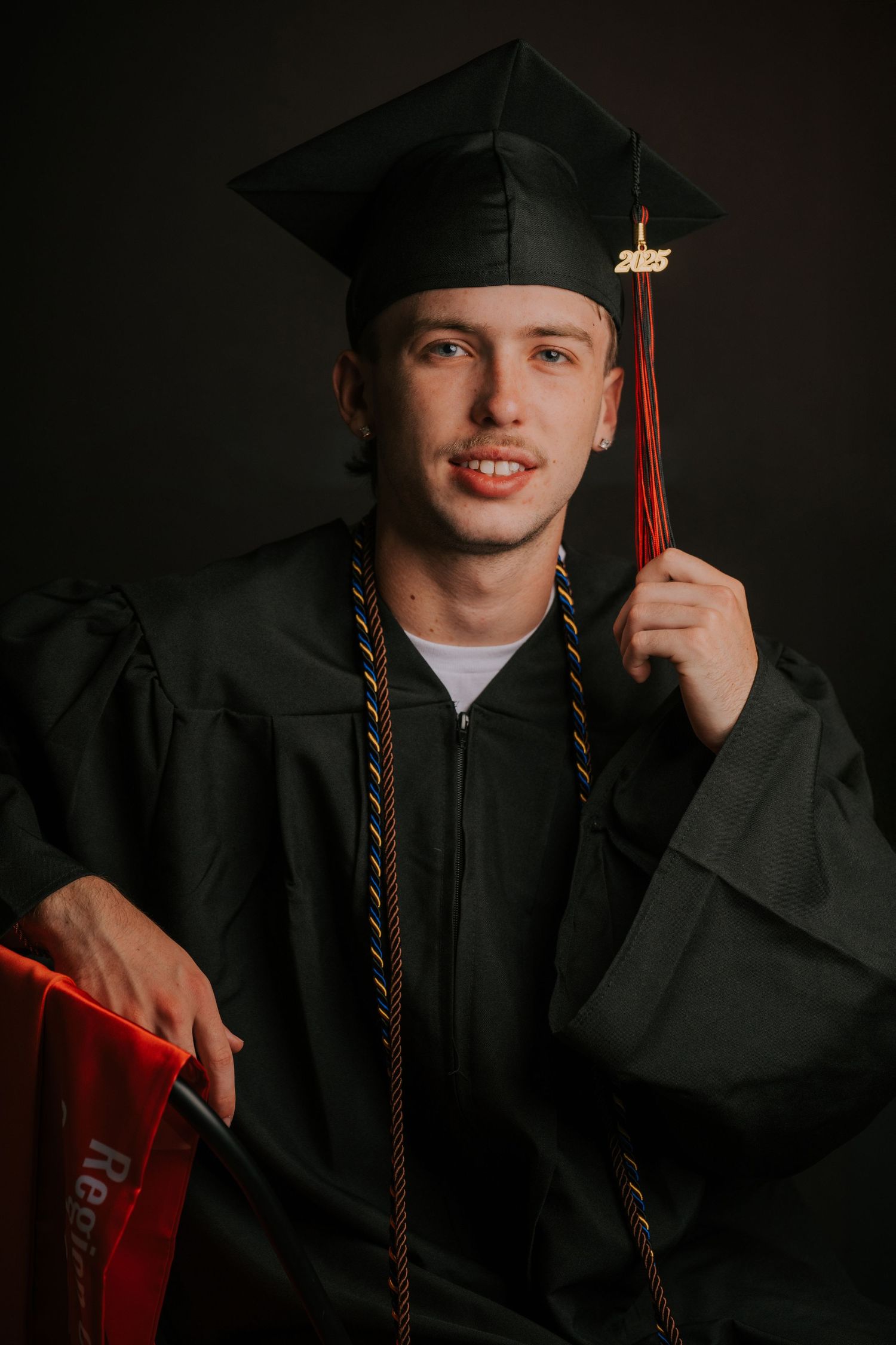 Graduate wearing black cap and gown with red tassel poses for series of graduation portraits.