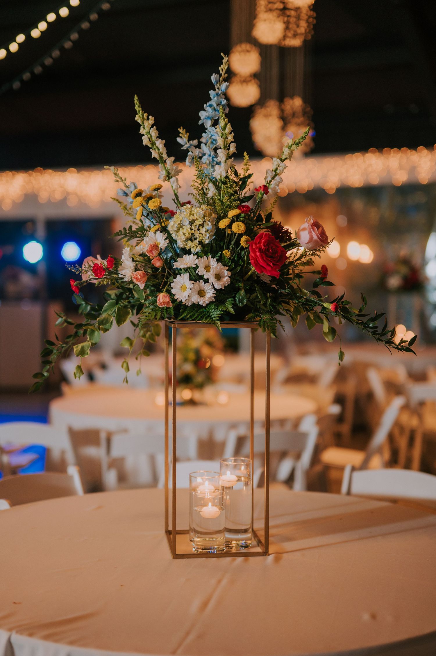 Elegant floral centerpieces with white and pink flowers on reception tables with warm lighting.