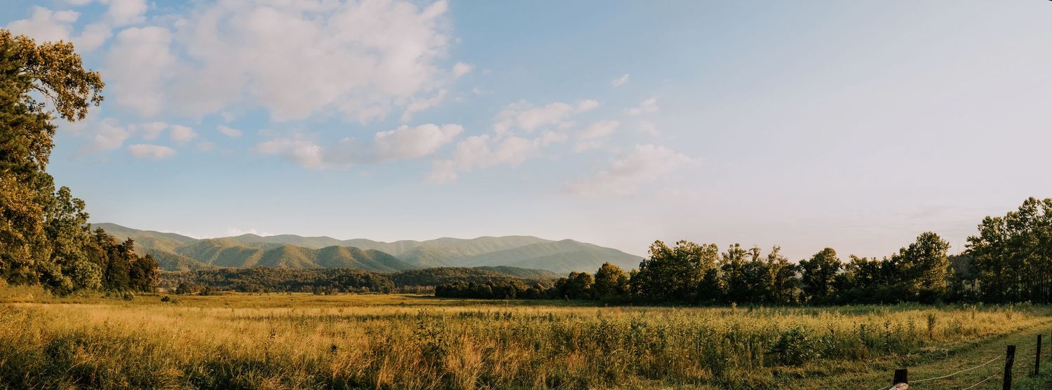 Wide panoramic view of rolling hills and farmland under puffy white clouds.