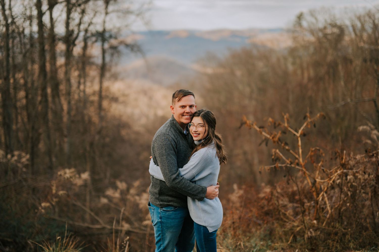 A couple shares intimate moments against a backdrop of misty mountains and bare winter trees.