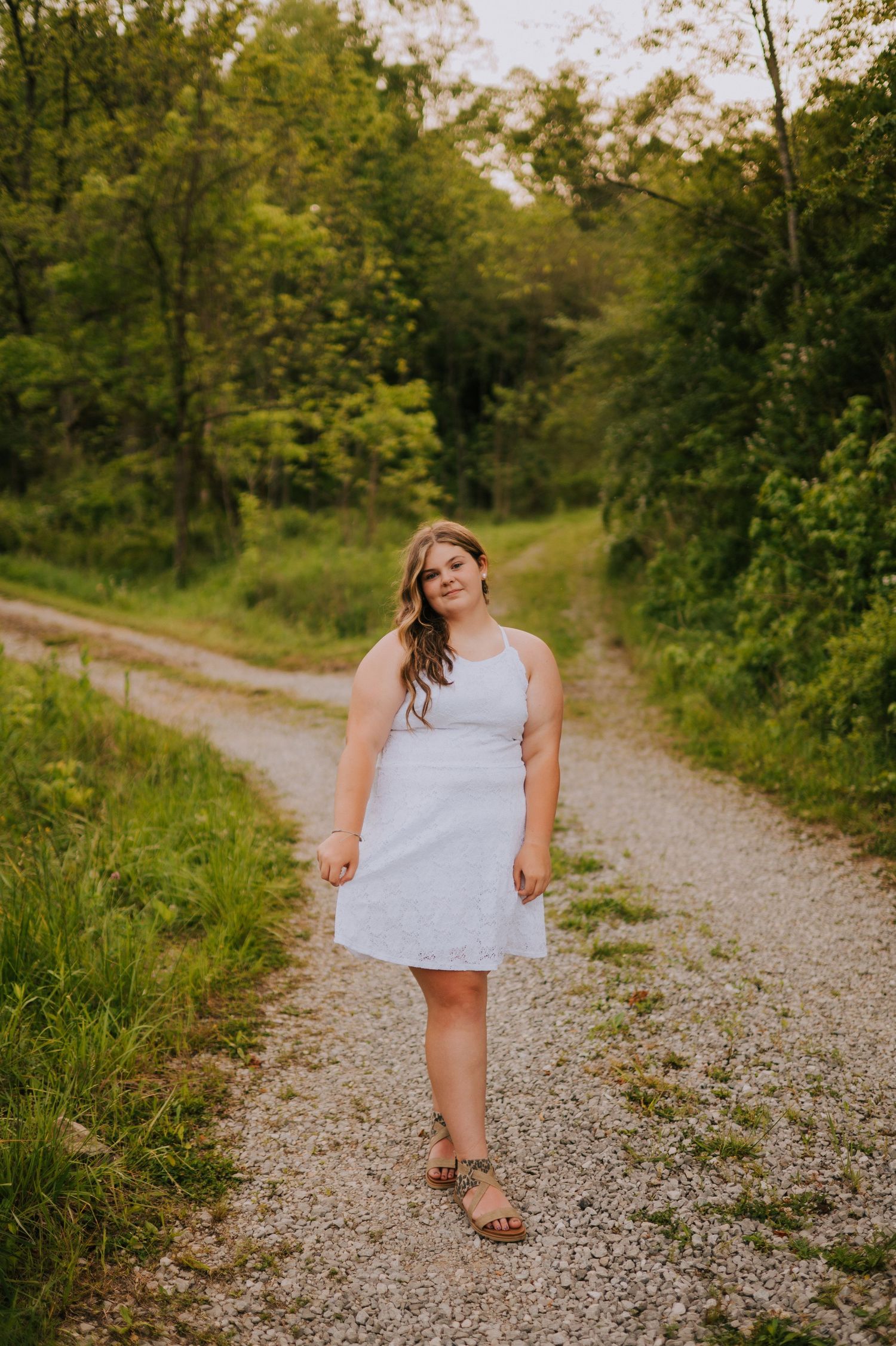 A person walks along a winding gravel path through lush summer greenery.