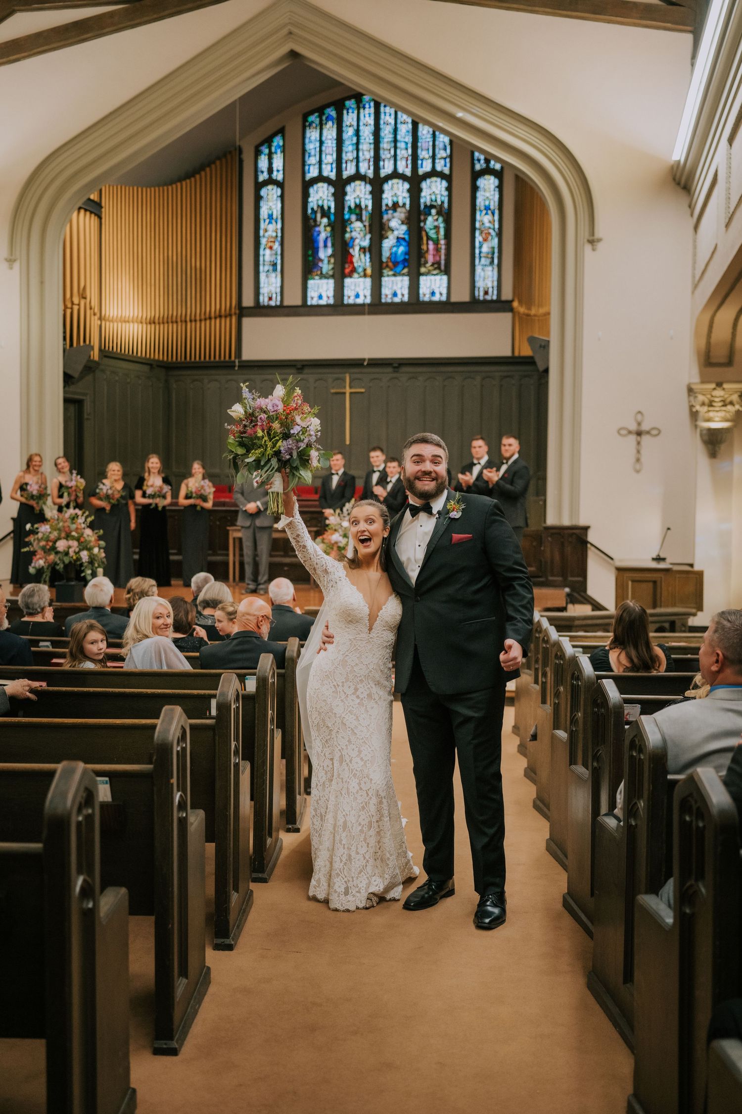 A joyful couple celebrates during their wedding ceremony in a church with stained glass windows and wooden pews.