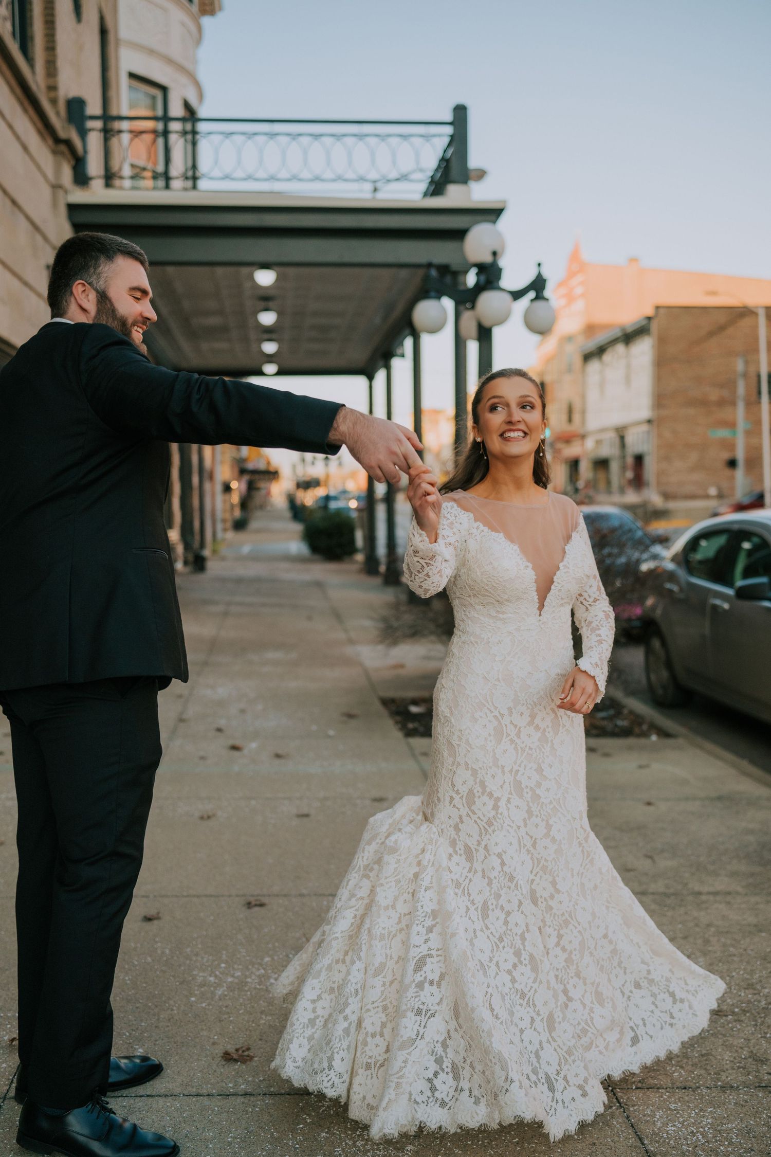 A bride and groom share a playful dance moment on a city street in front of historic buildings.
