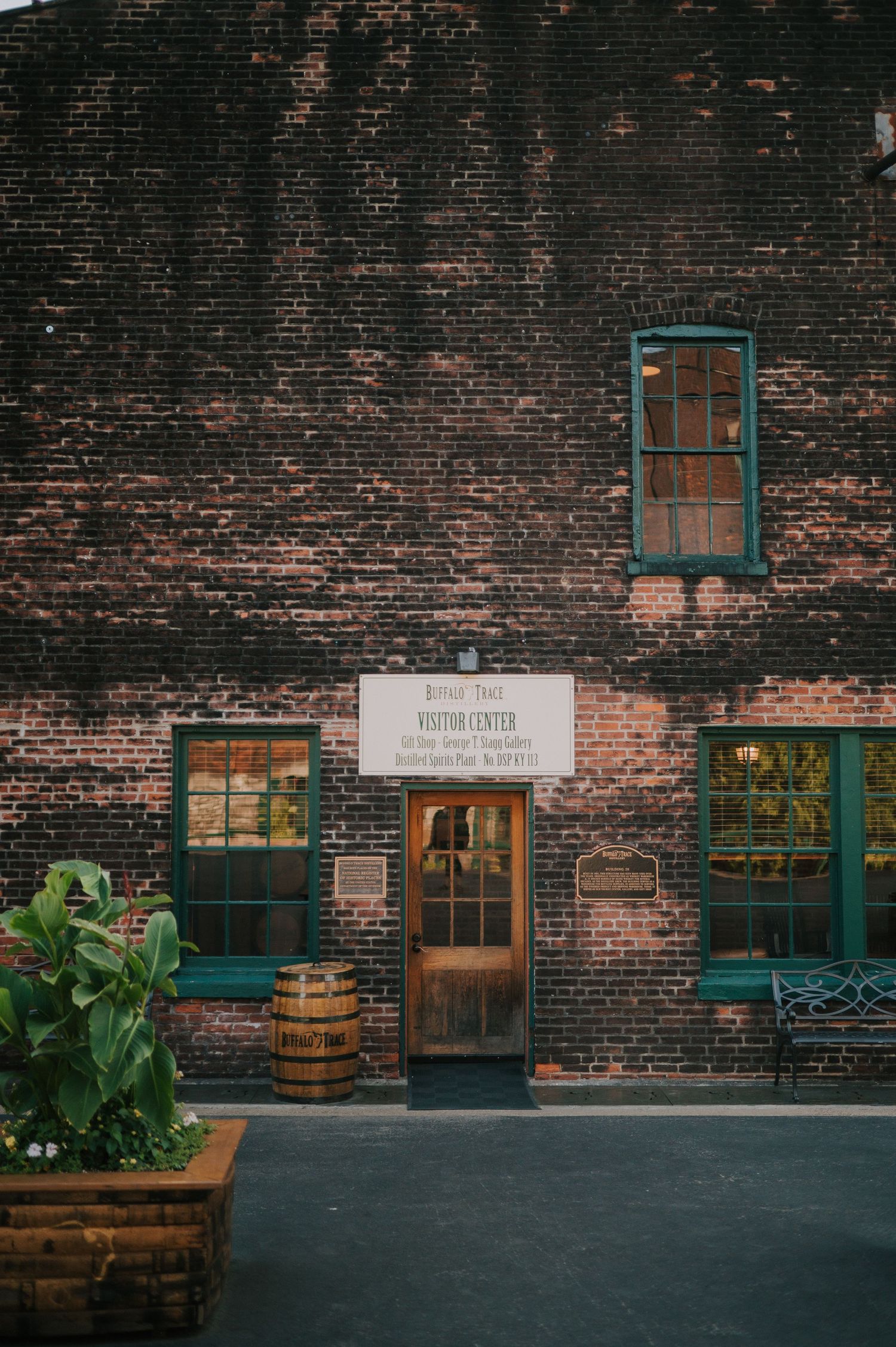 Rustic brick wall exterior with vintage wooden barrels and green-trimmed windows.