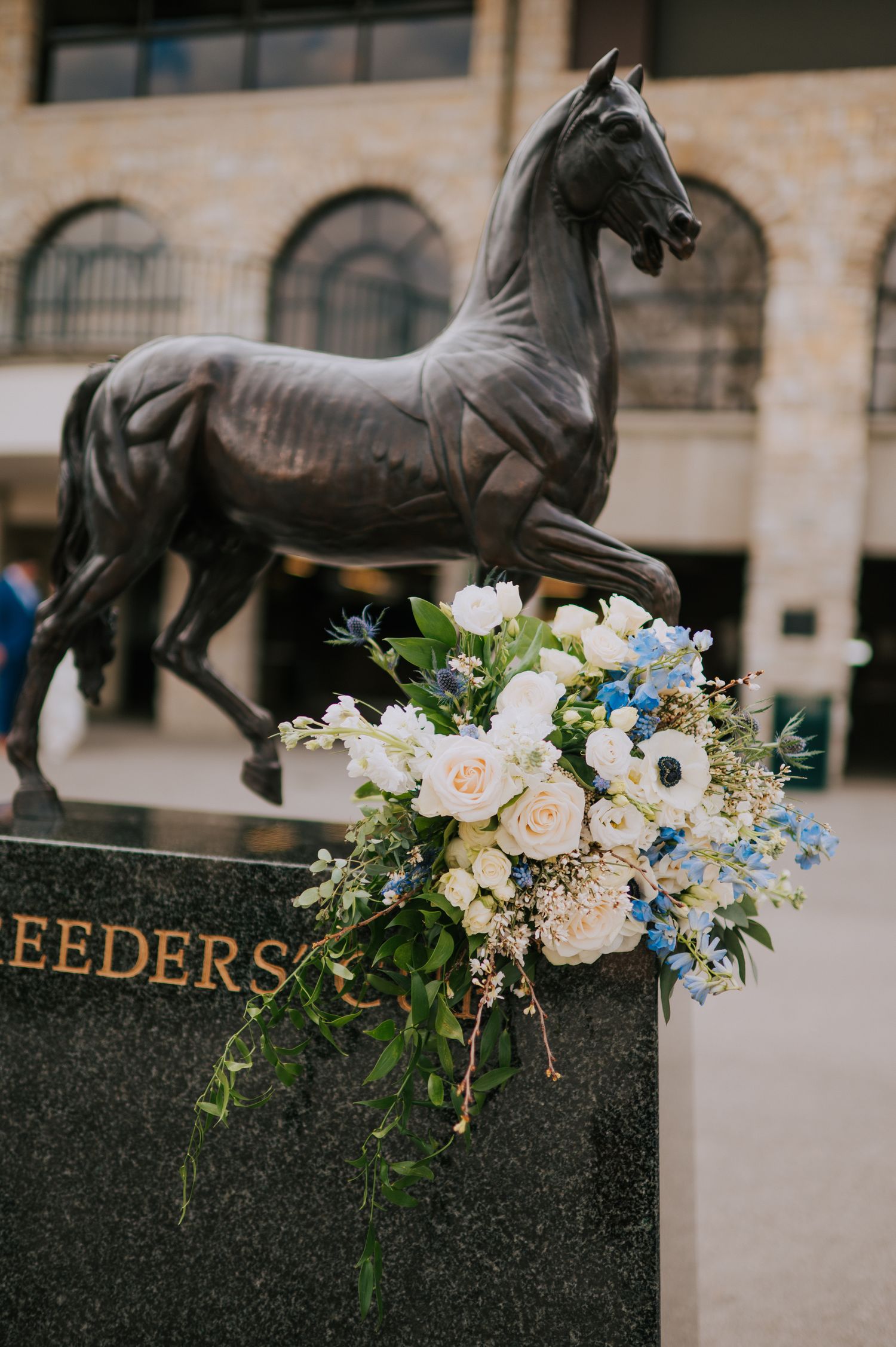 Wedding floral arrangement with white and blue flowers decorating bronze horse statues.