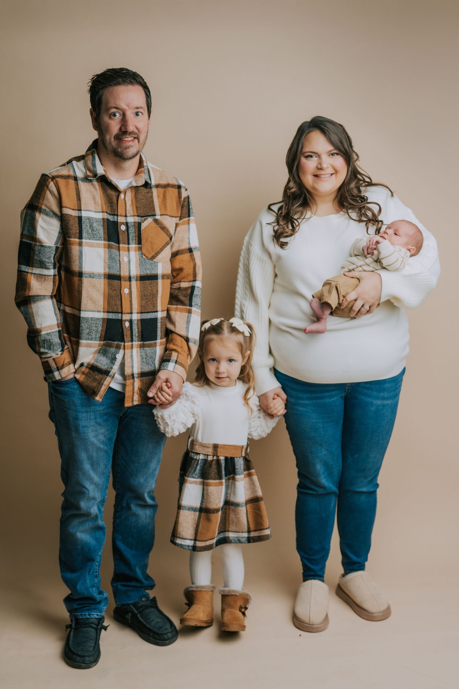 Family wearing coordinated outfits in plaid and denim poses for studio portrait.